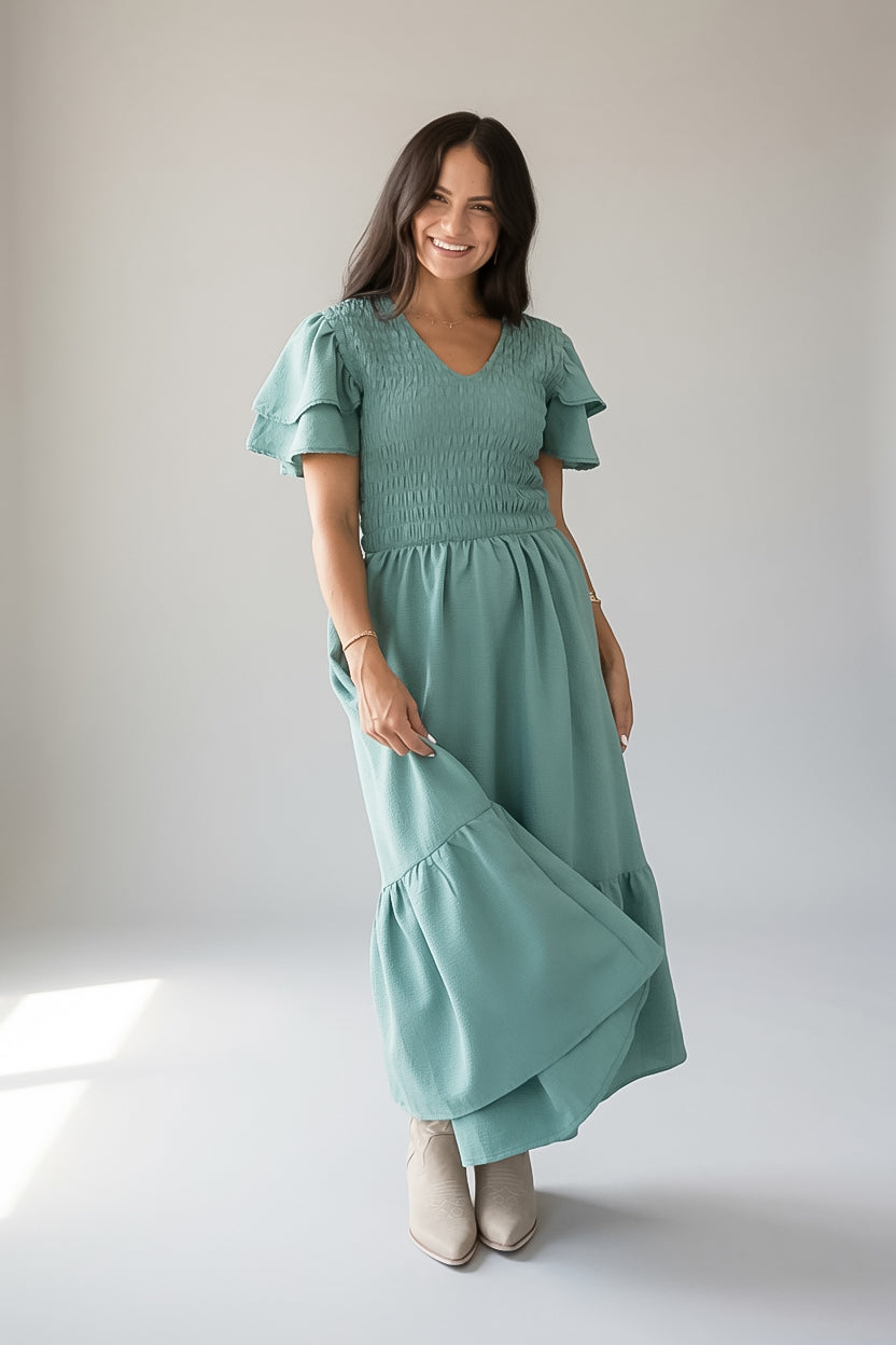 A woman wearing a sage green tiered maxi dress with ruffled short sleeves and smocked detailing
