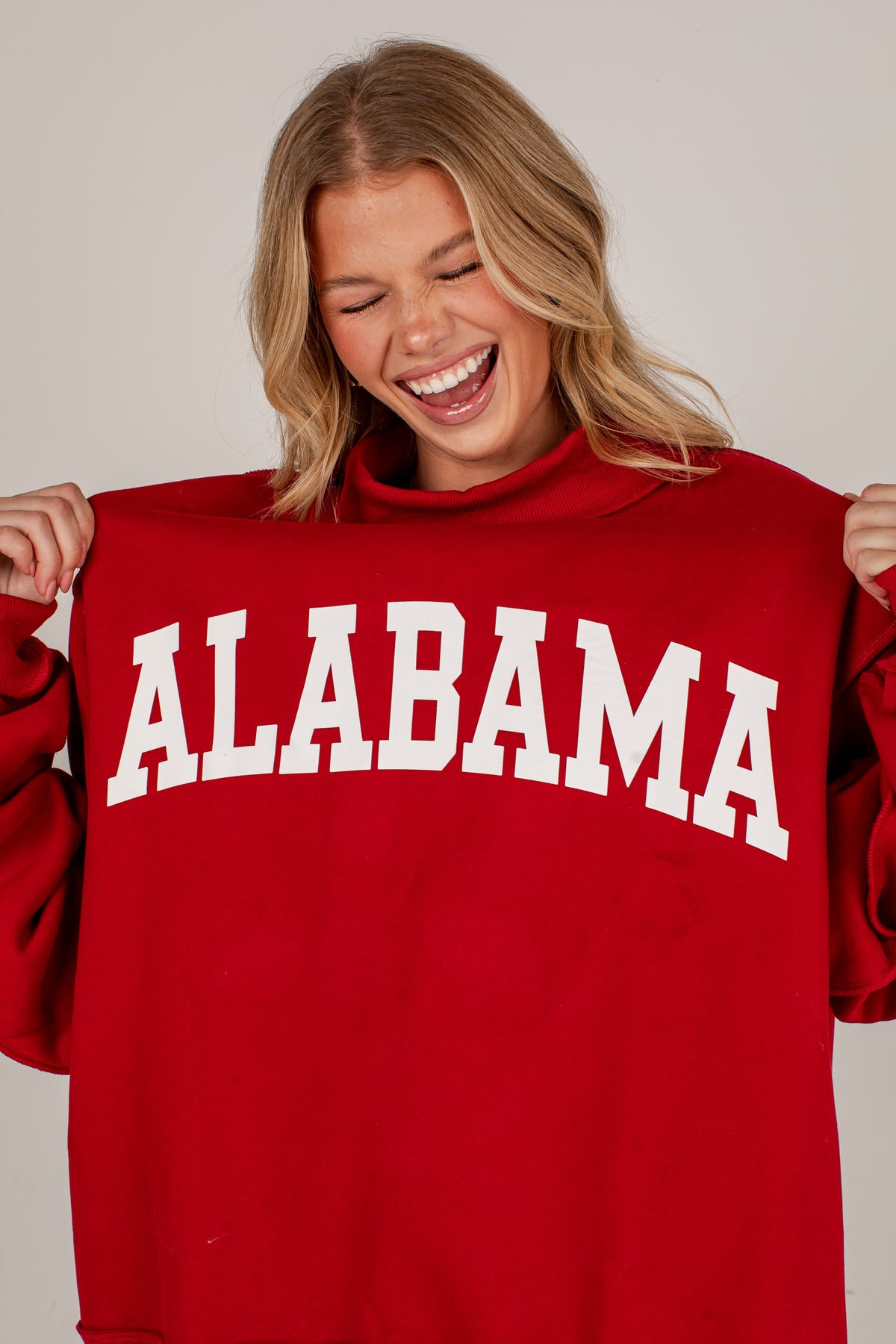 A woman smiling and holding up a red sweatshirt with &