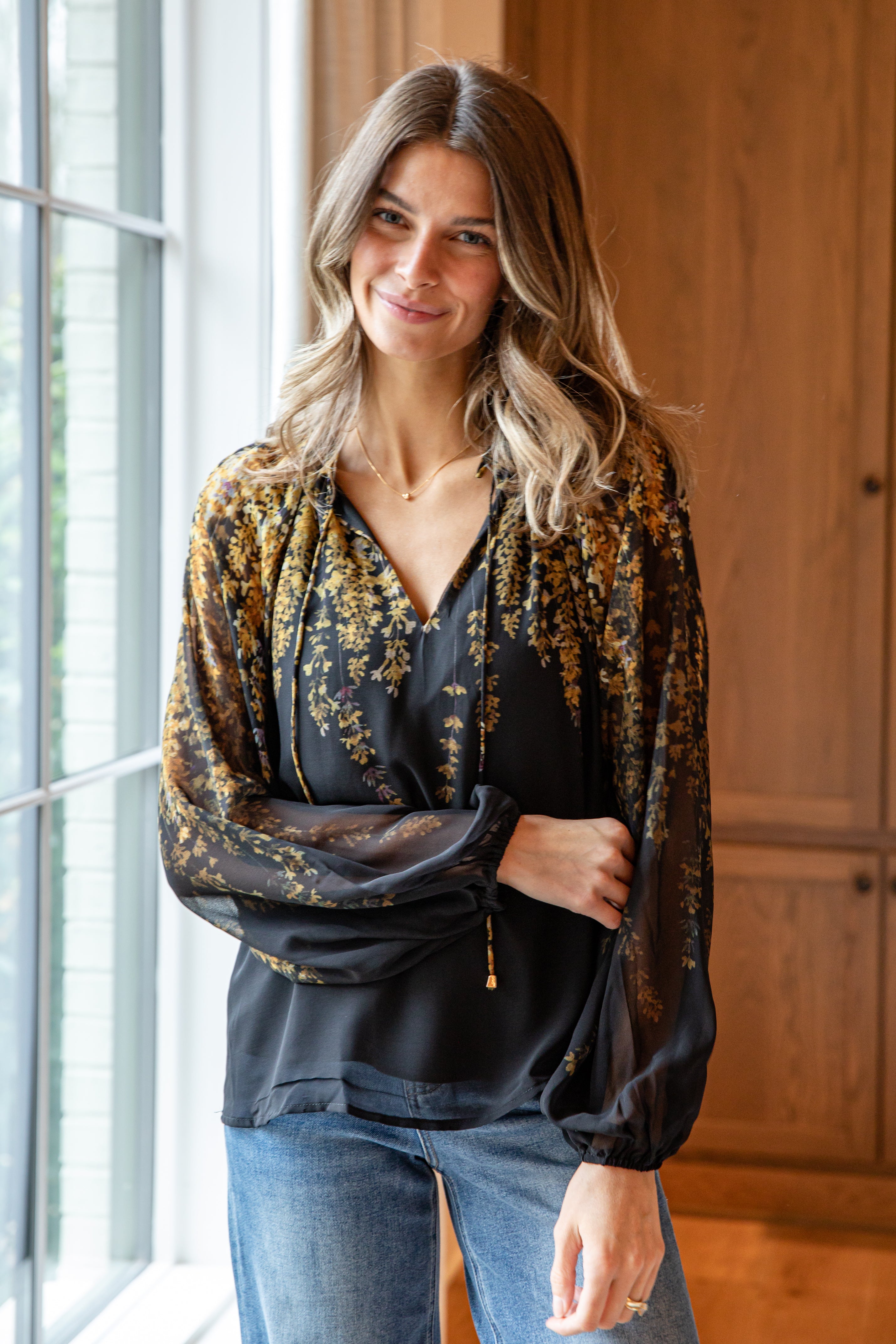 Woman wearing a floral blouse and jeans standing indoors.