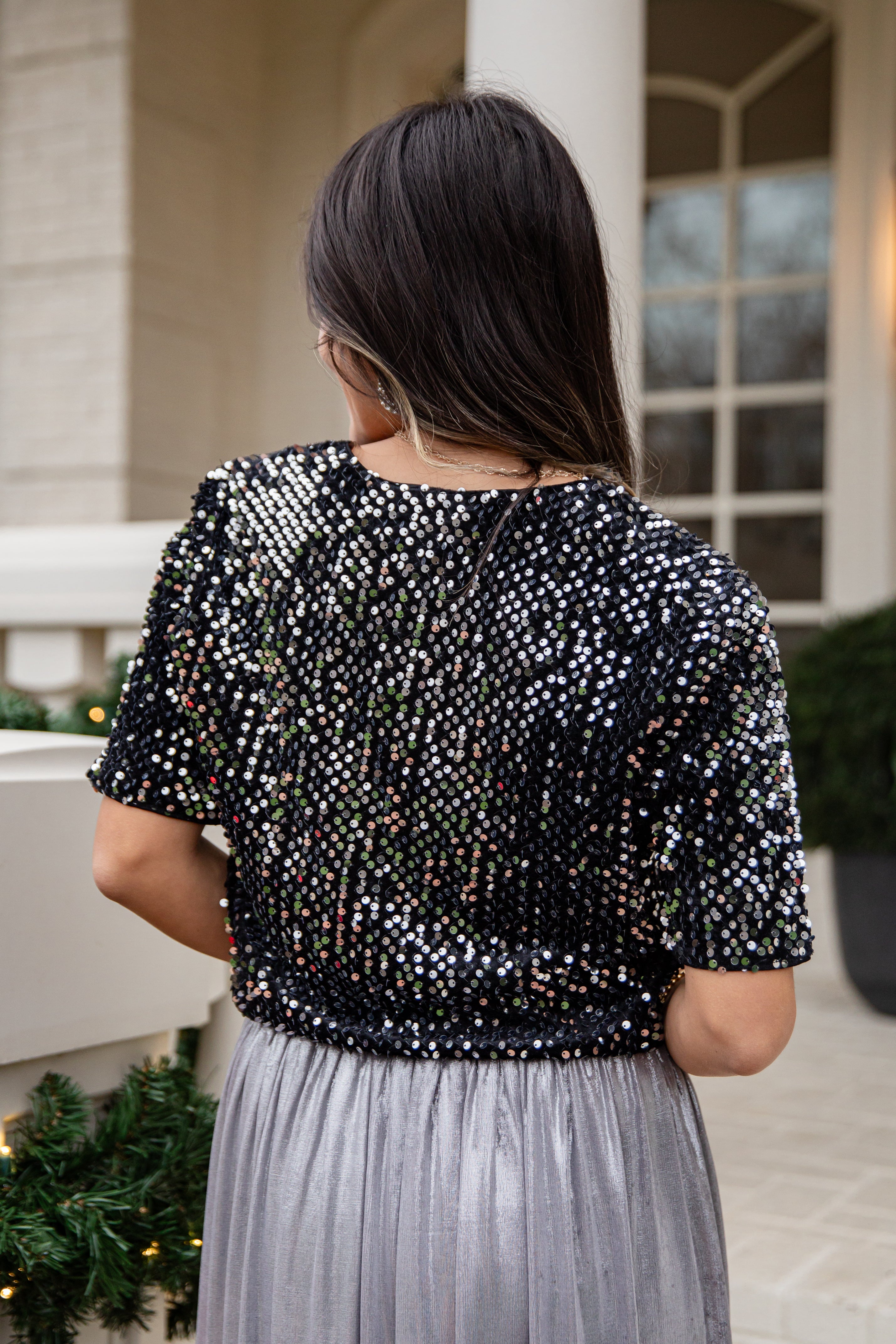 Woman wearing a black sequin top and gray skirt outdoors.