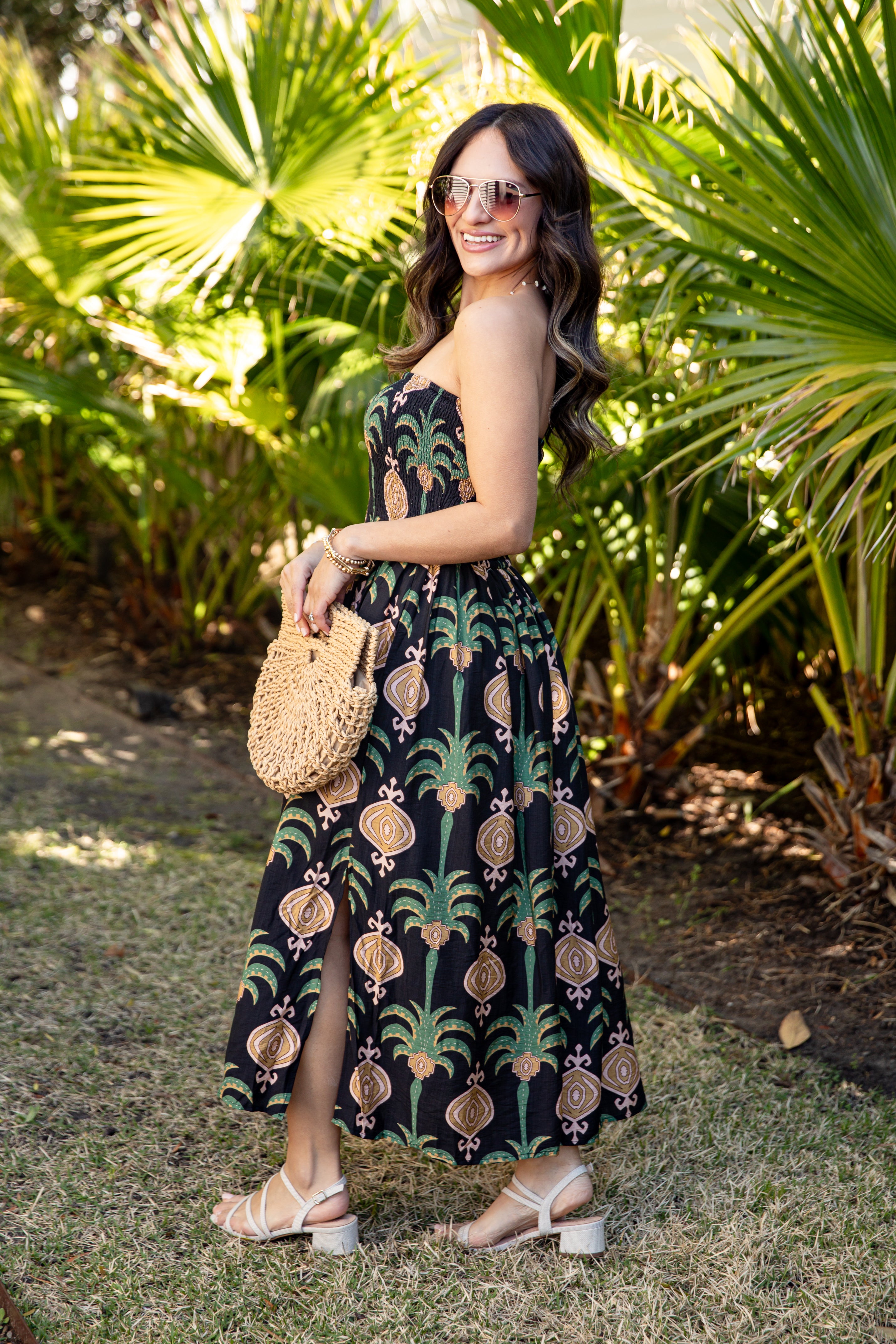 Woman in a patterned dress standing in a tropical setting with palm trees.