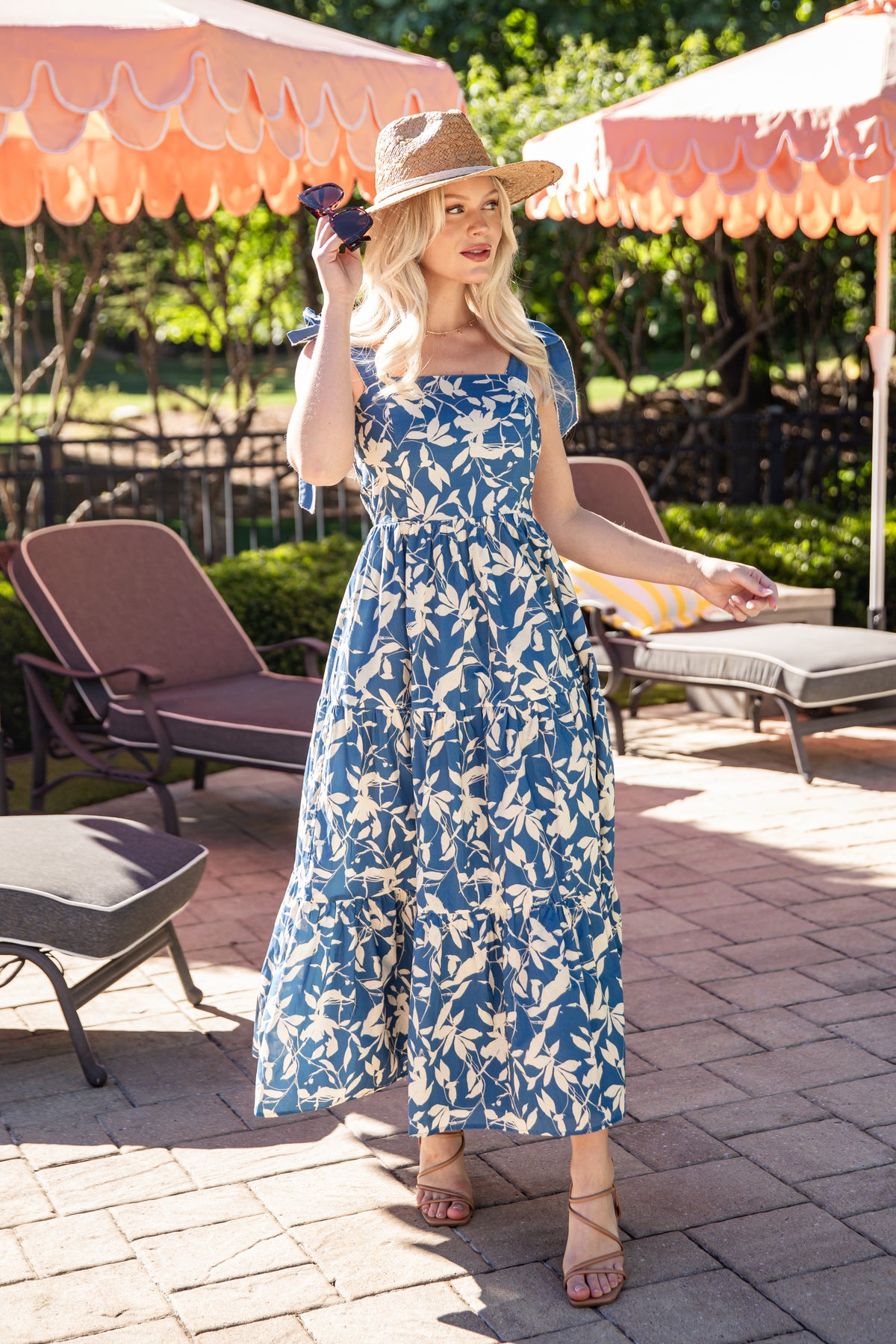 Woman in a blue floral dress standing outdoors under pink umbrellas.
