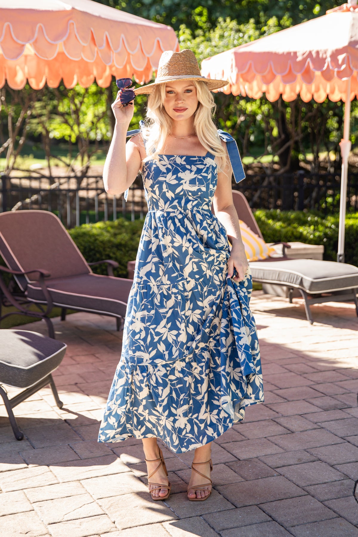 Woman in a blue floral dress standing outdoors under umbrellas.