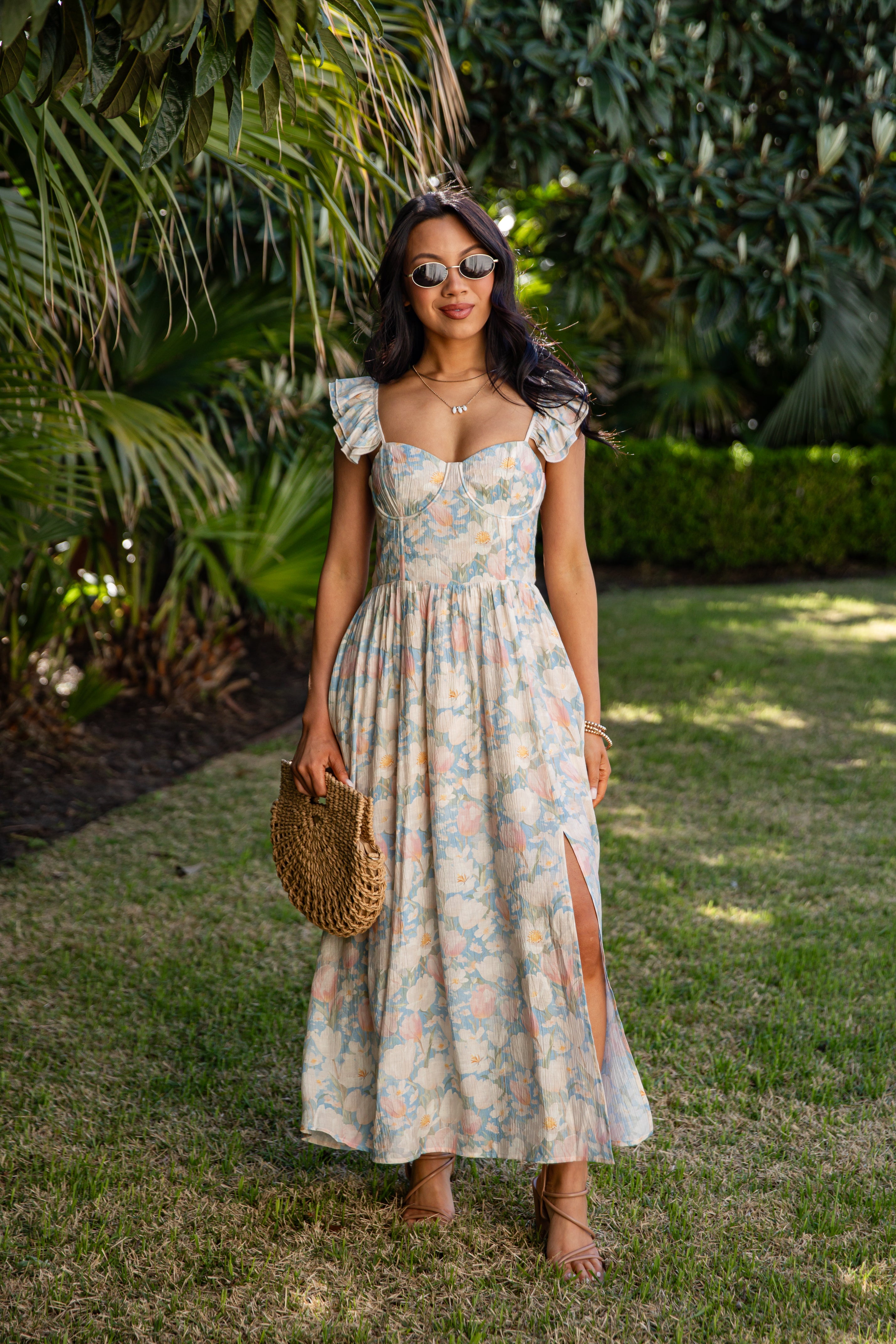 Woman in a floral dress standing outdoors with greenery in the background