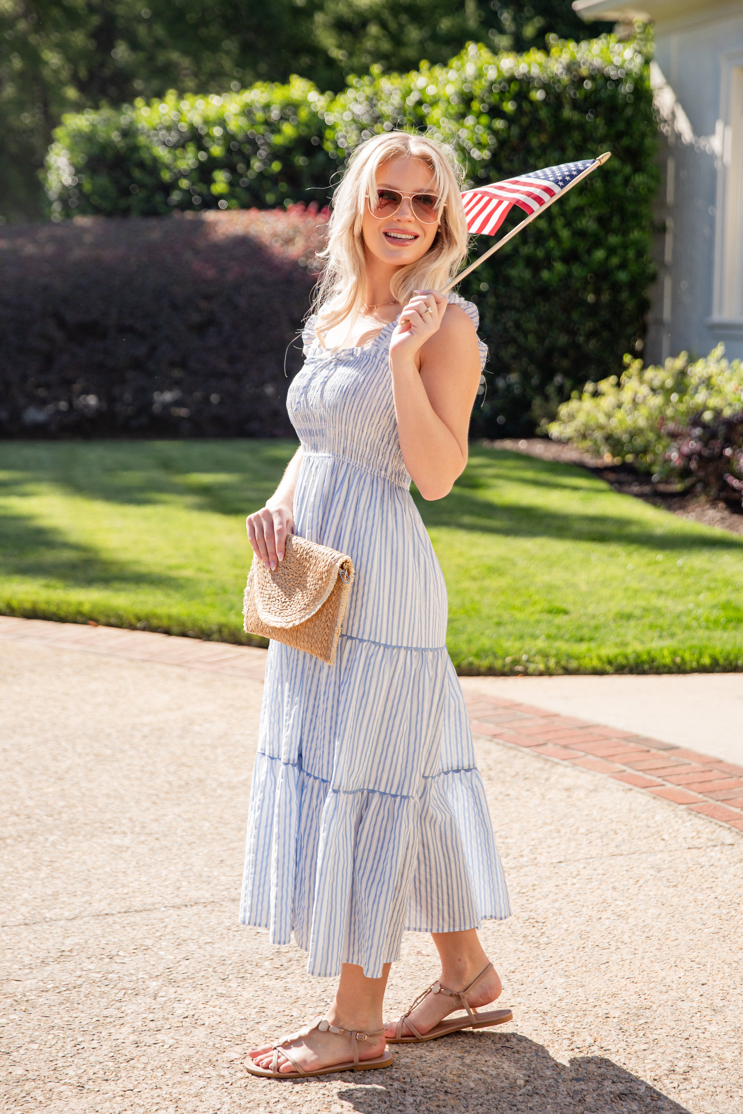 Woman in a blue striped dress holding an American flag outdoors.