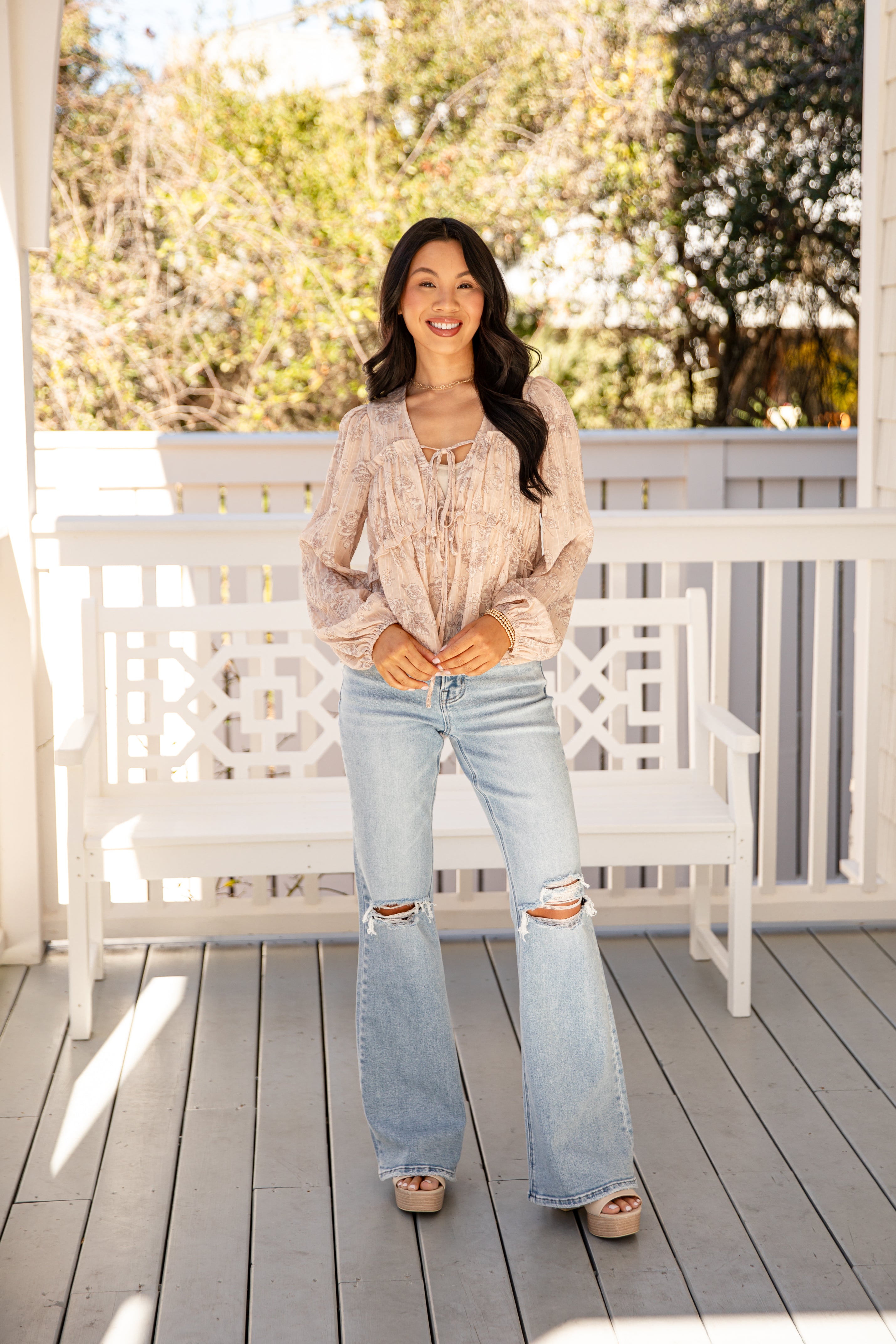 Woman standing on a wooden deck with a white bench and greenery in the background