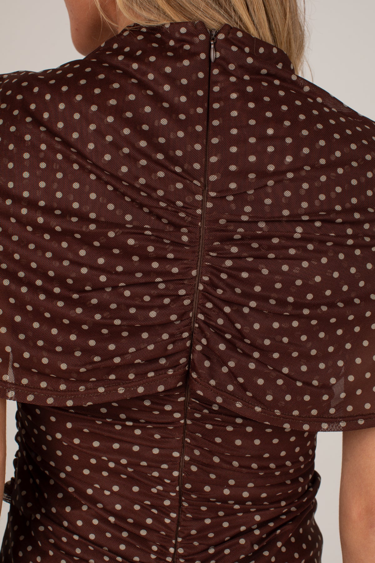 Close-up back view of a woman wearing a brown sheer mesh top with beige polka dots and ruched detailing.