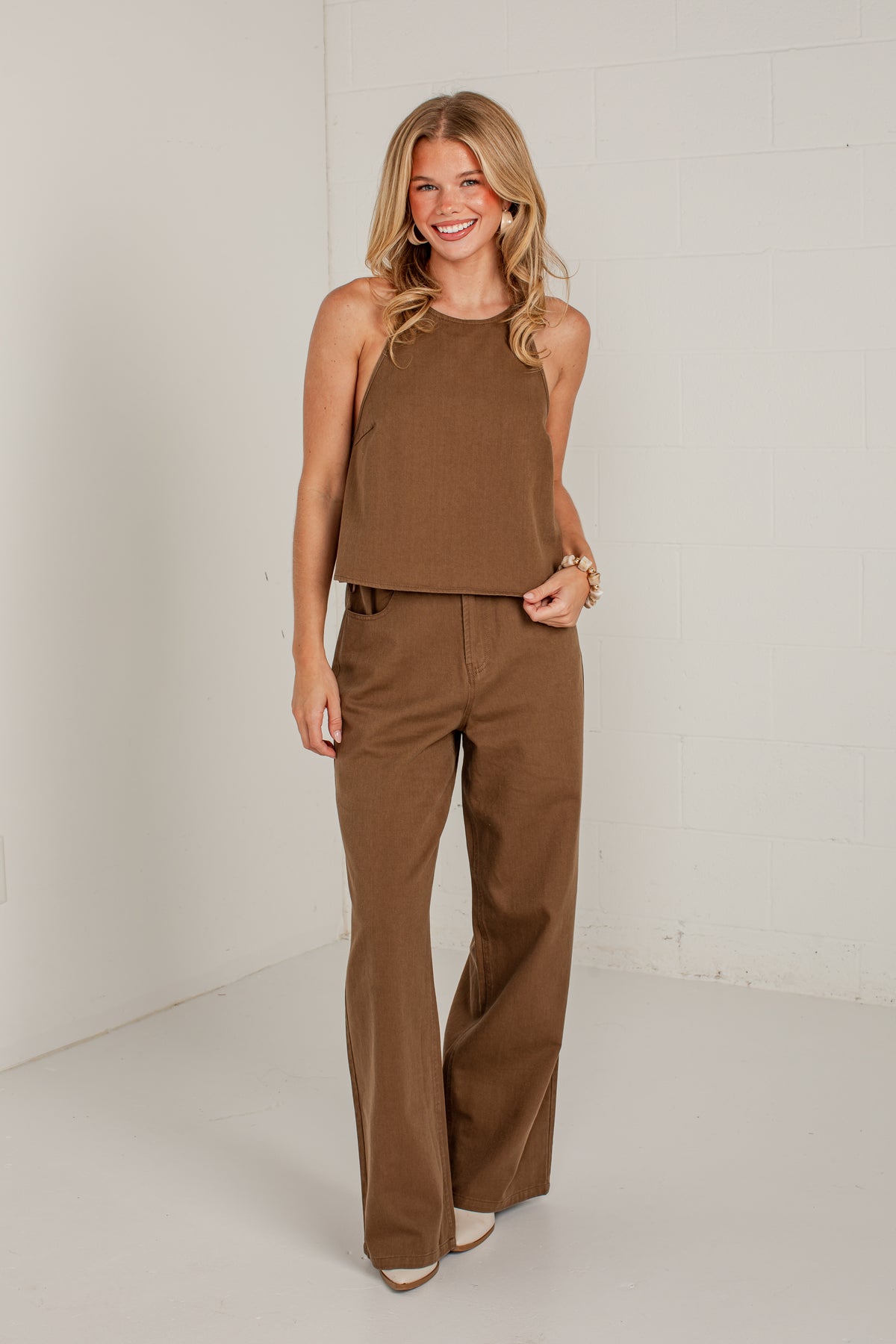A woman modeling a brown sleeveless crop top and matching wide-leg pants against a white studio wall.