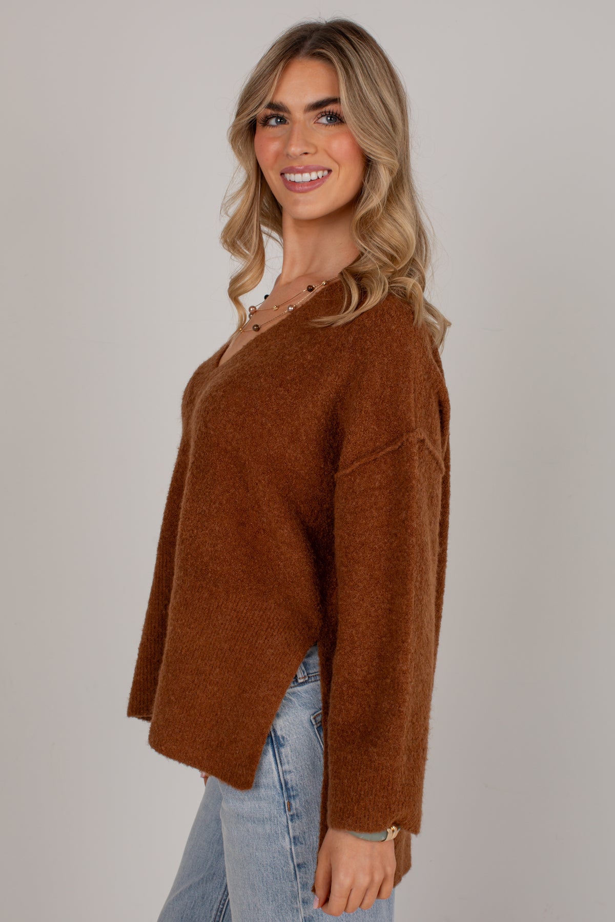 A woman wearing a brown fuzzy knit sweater and light blue jeans, photographed against a plain light gray studio background.