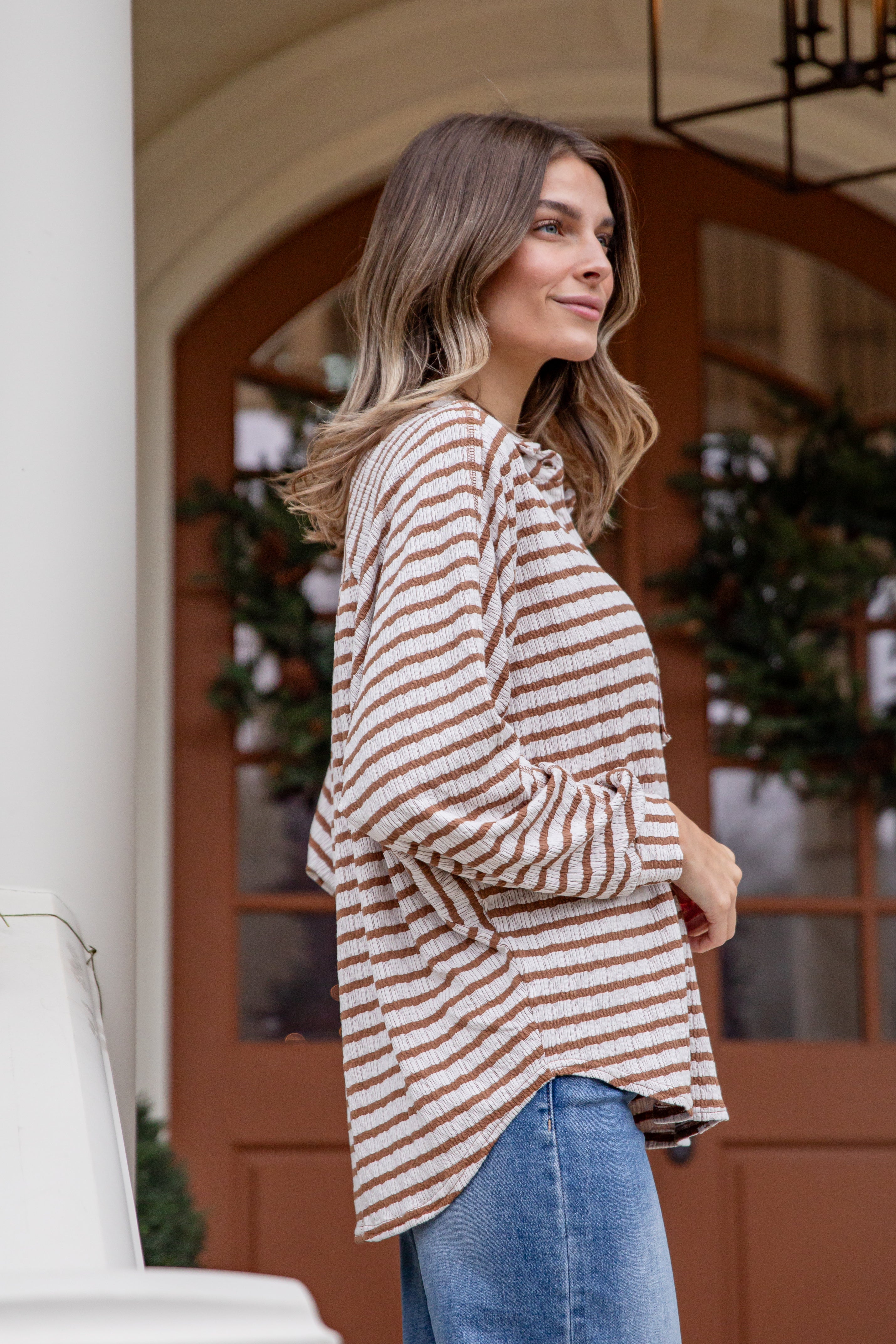 Woman wearing a striped sweater and jeans standing in front of a door with decorative elements.