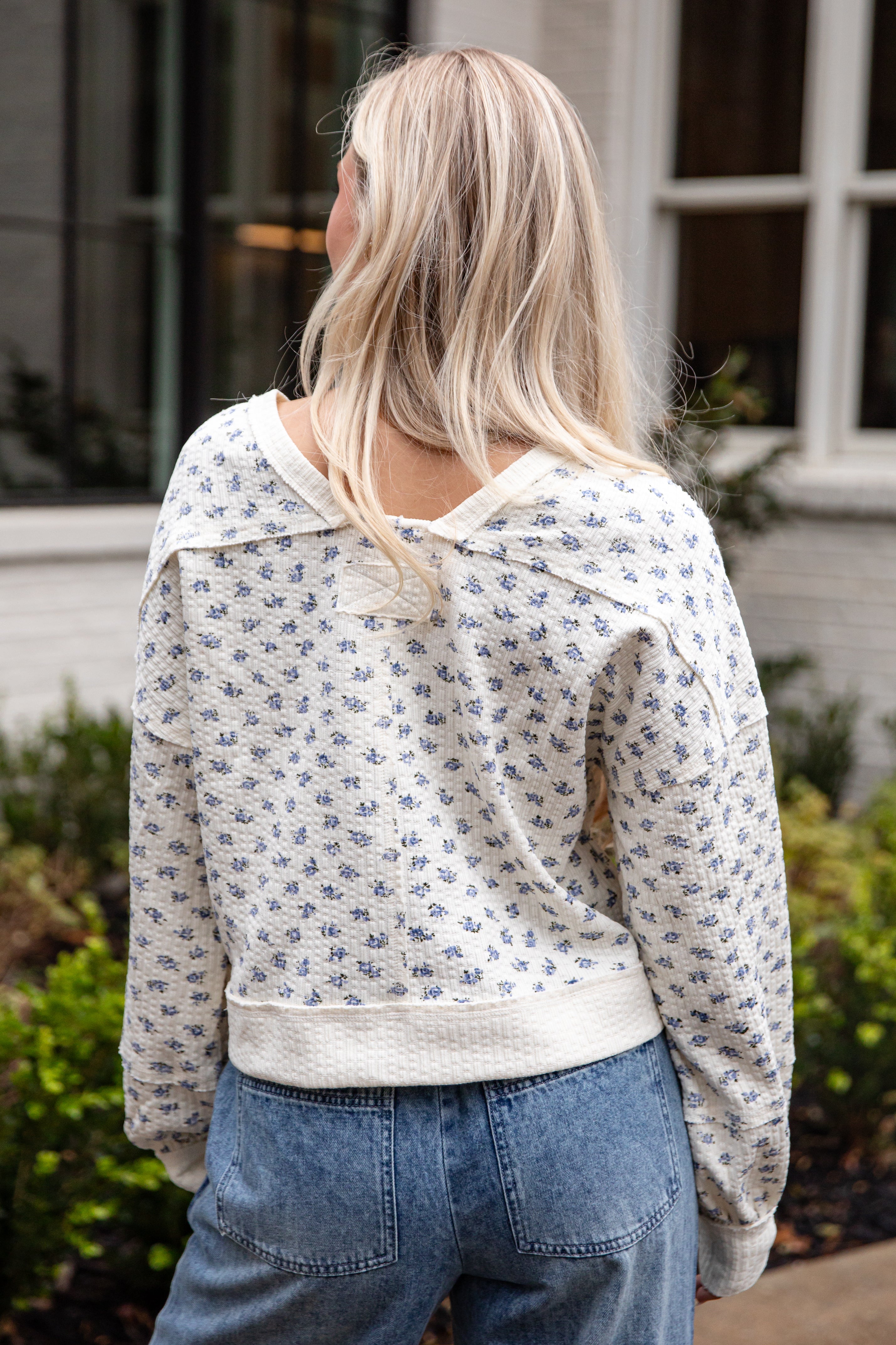 Person wearing a floral-patterned jacket and blue jeans outdoors.