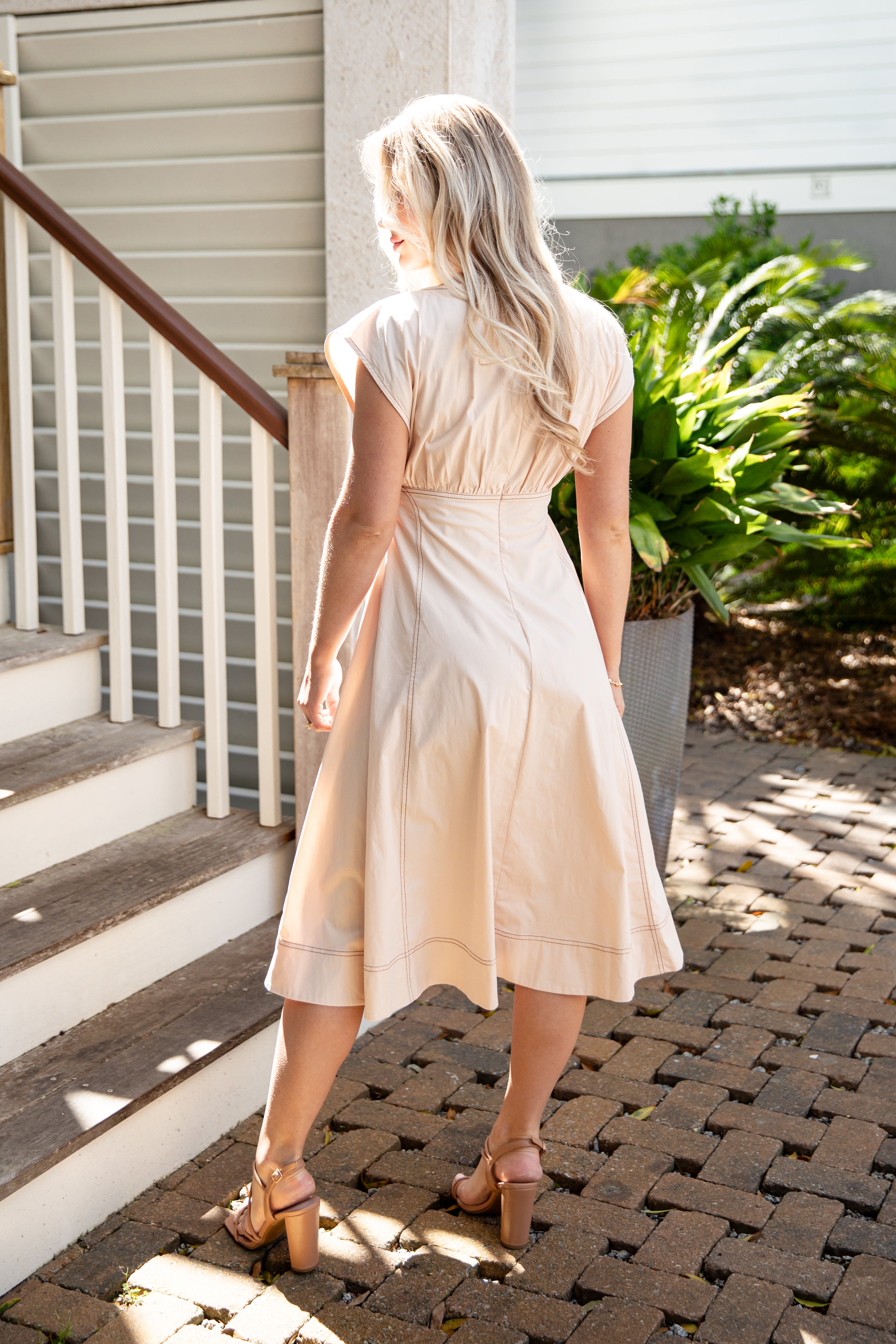 Woman in a beige dress standing on a patio with plants and steps in the background