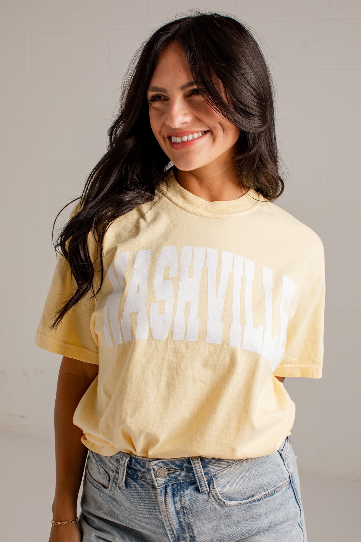 A woman wearing a pale yellow graphic t-shirt with &