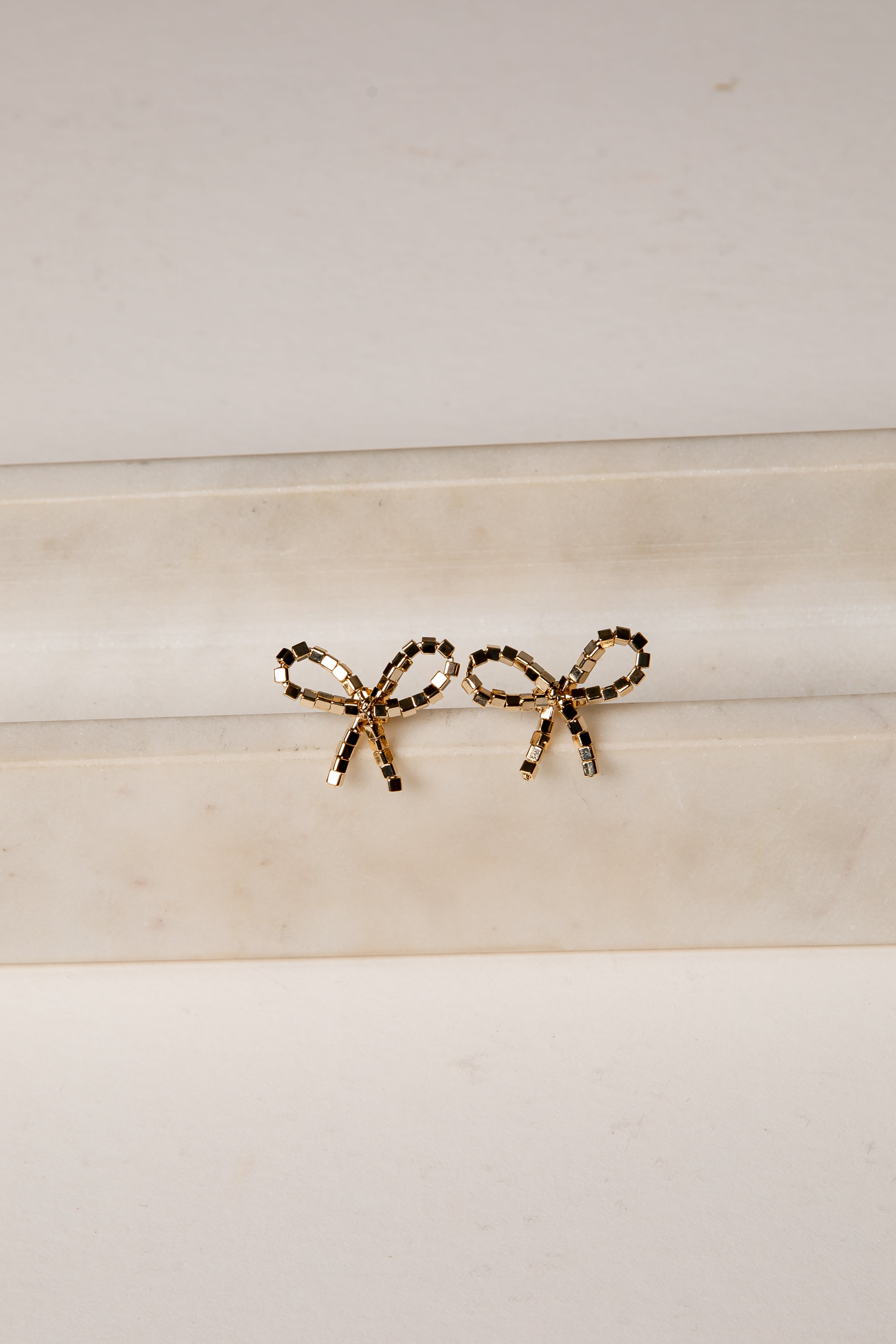 Gold bow-shaped earrings on a marble surface