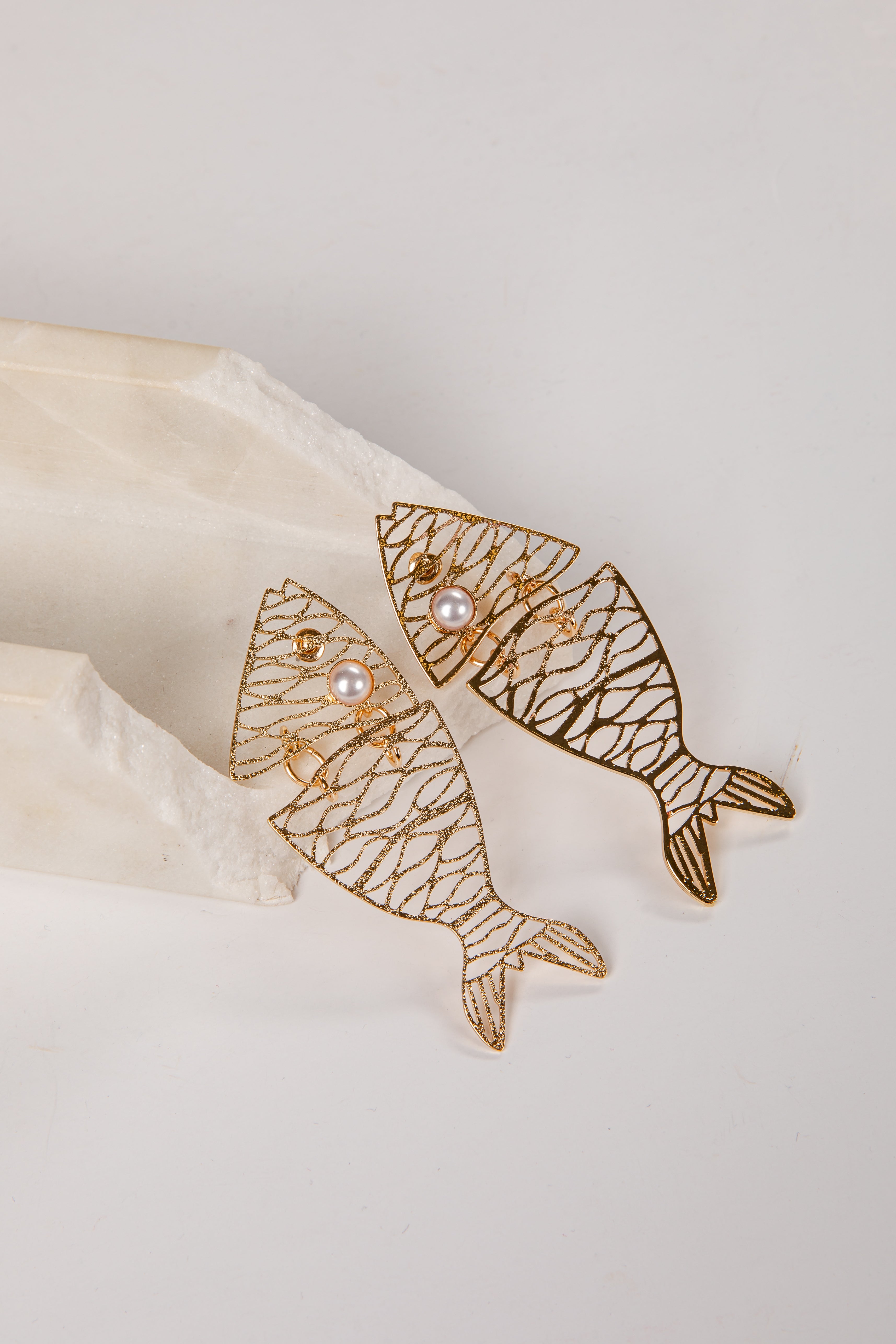 Gold fish-shaped earrings with pearl centers on a light background