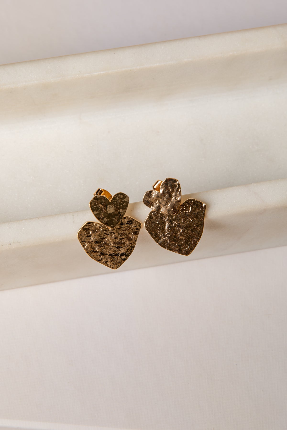 Heart-shaped gold earrings on a white marble surface
