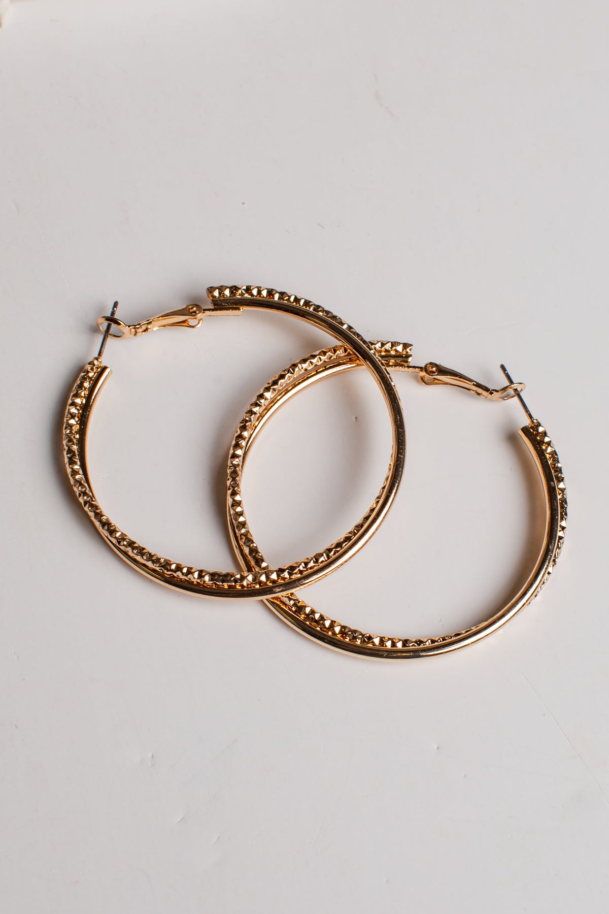 A pair of gold-tone hoop earrings with a textured, beaded outer edge and solid inner bands, displayed on a clean white background.