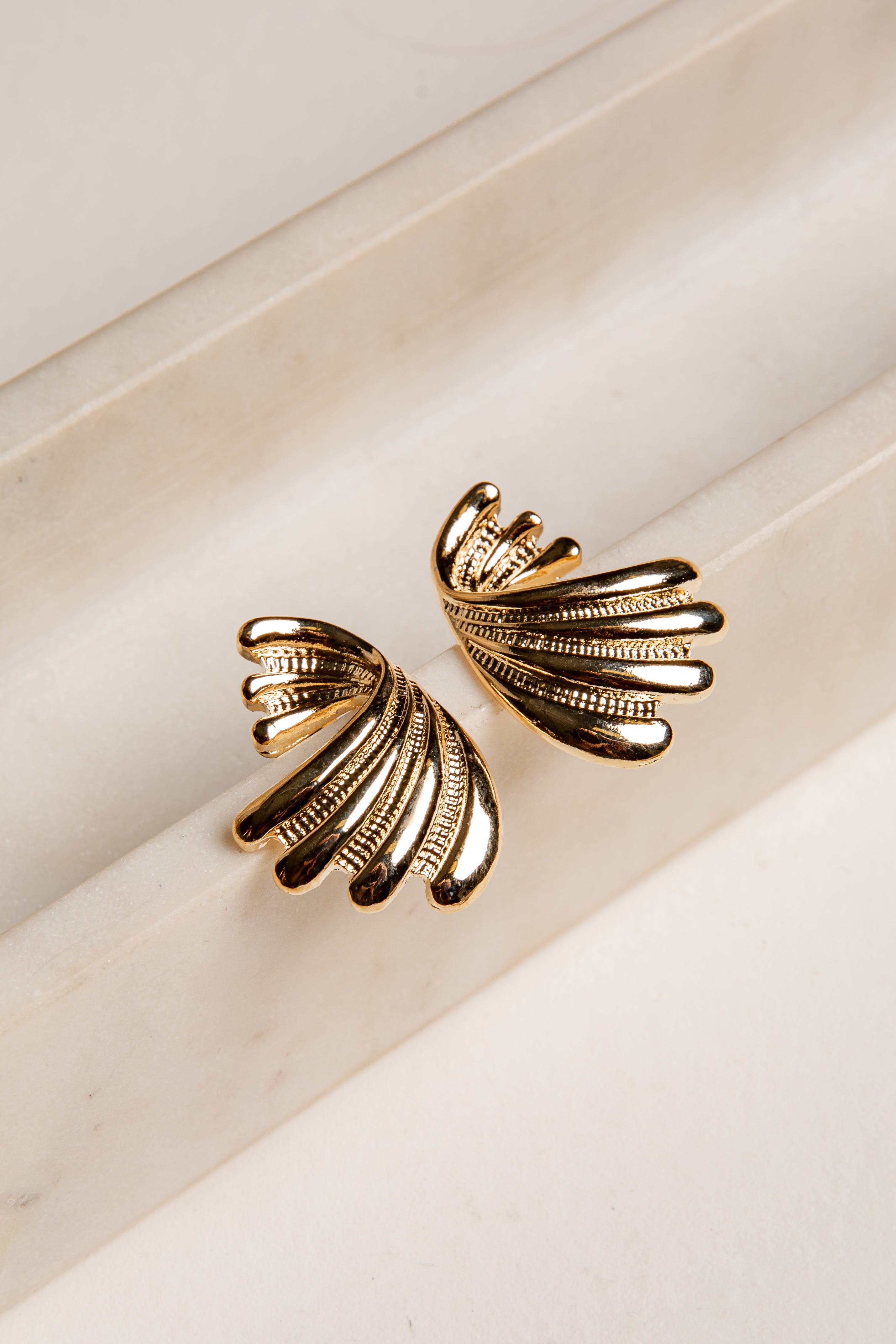 Gold leaf-shaped earrings on a light beige background