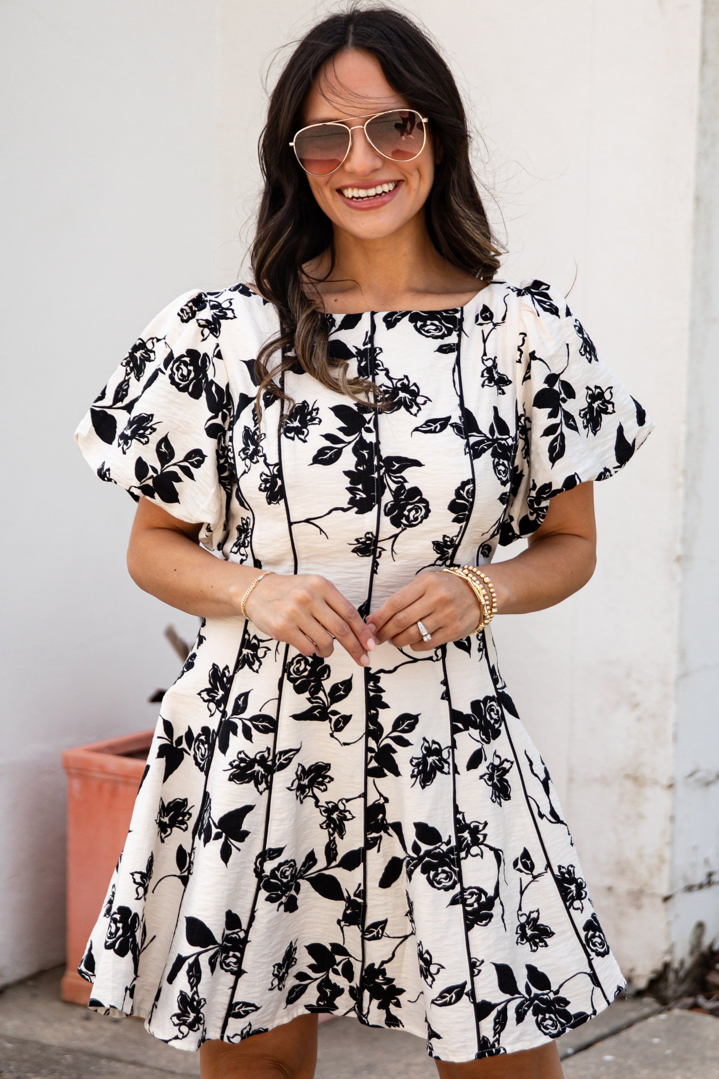 Woman wearing a black floral dress standing against a white wall.