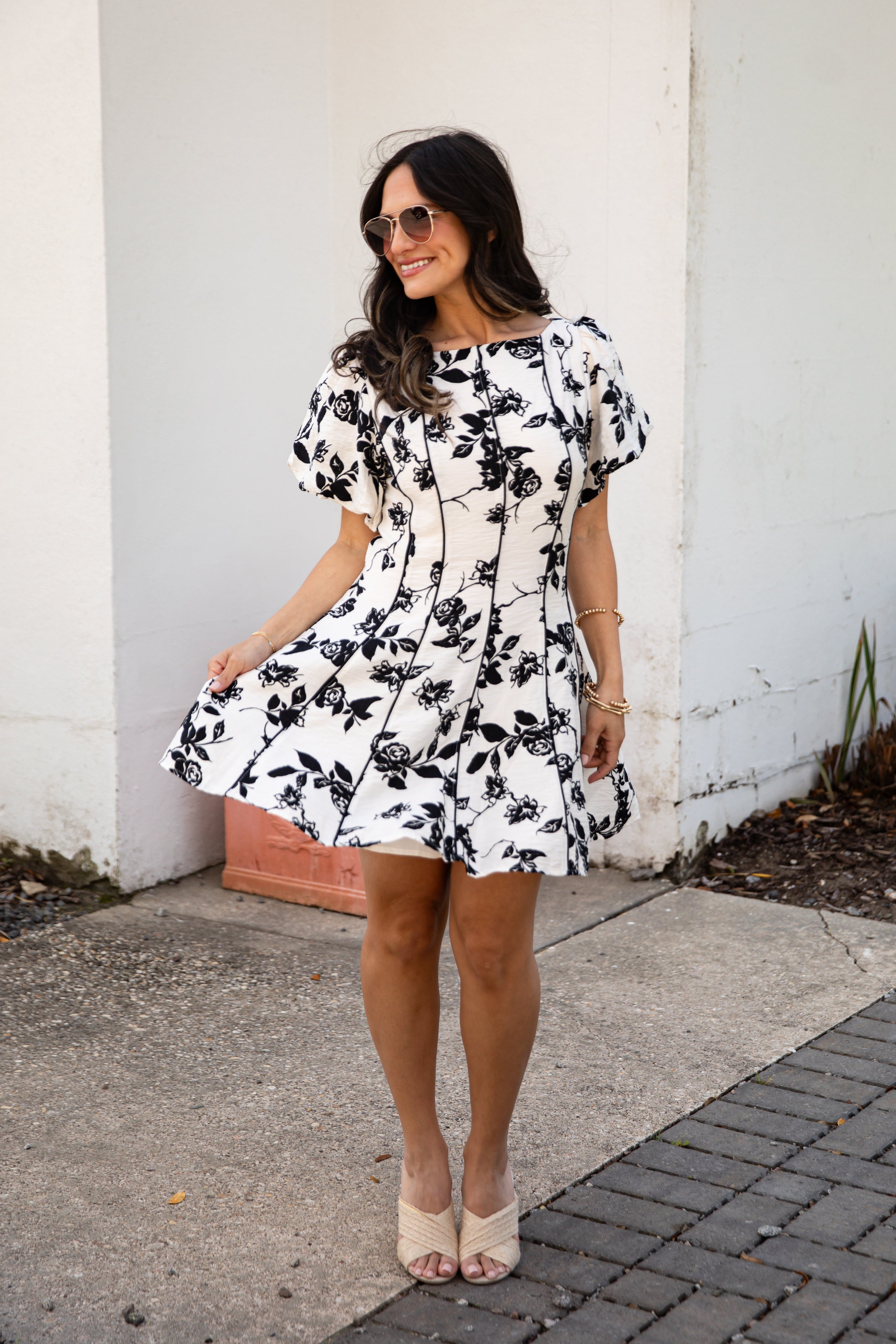 Woman wearing a black and white floral dress standing against a white wall.