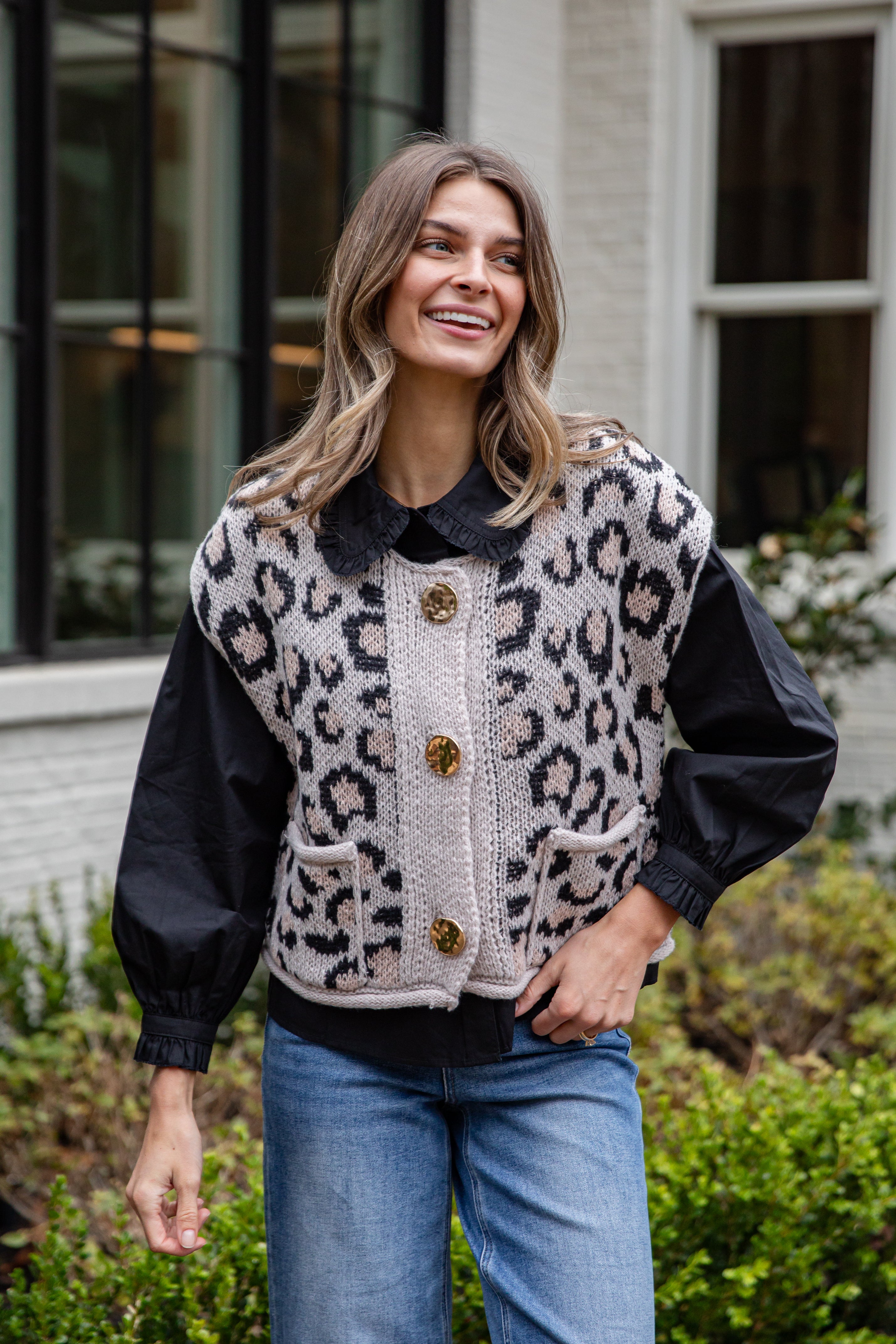 Woman wearing a leopard print vest with black sleeves and collar, standing outdoors.