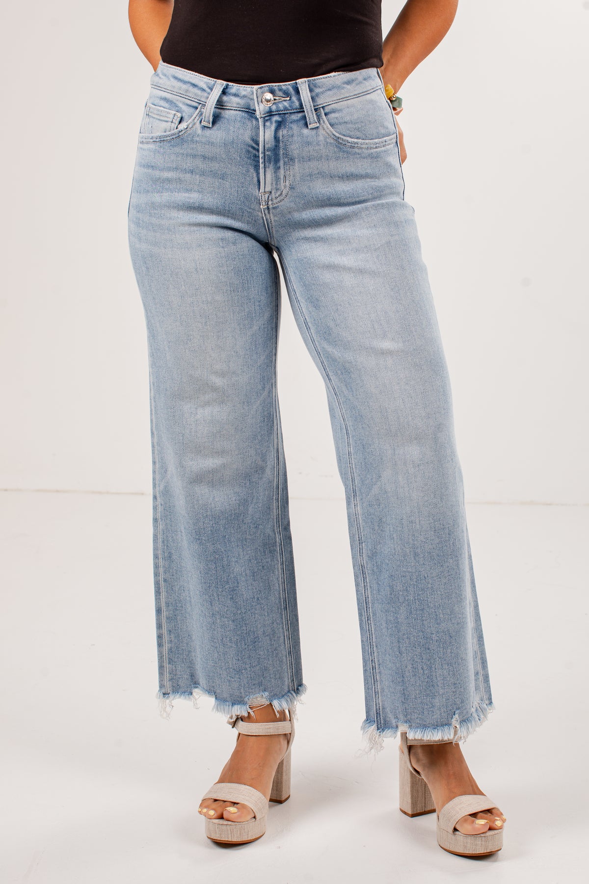 A person wearing light-wash wide-leg cropped jeans with a raw frayed hem, paired with beige platform sandals against a plain light background.
