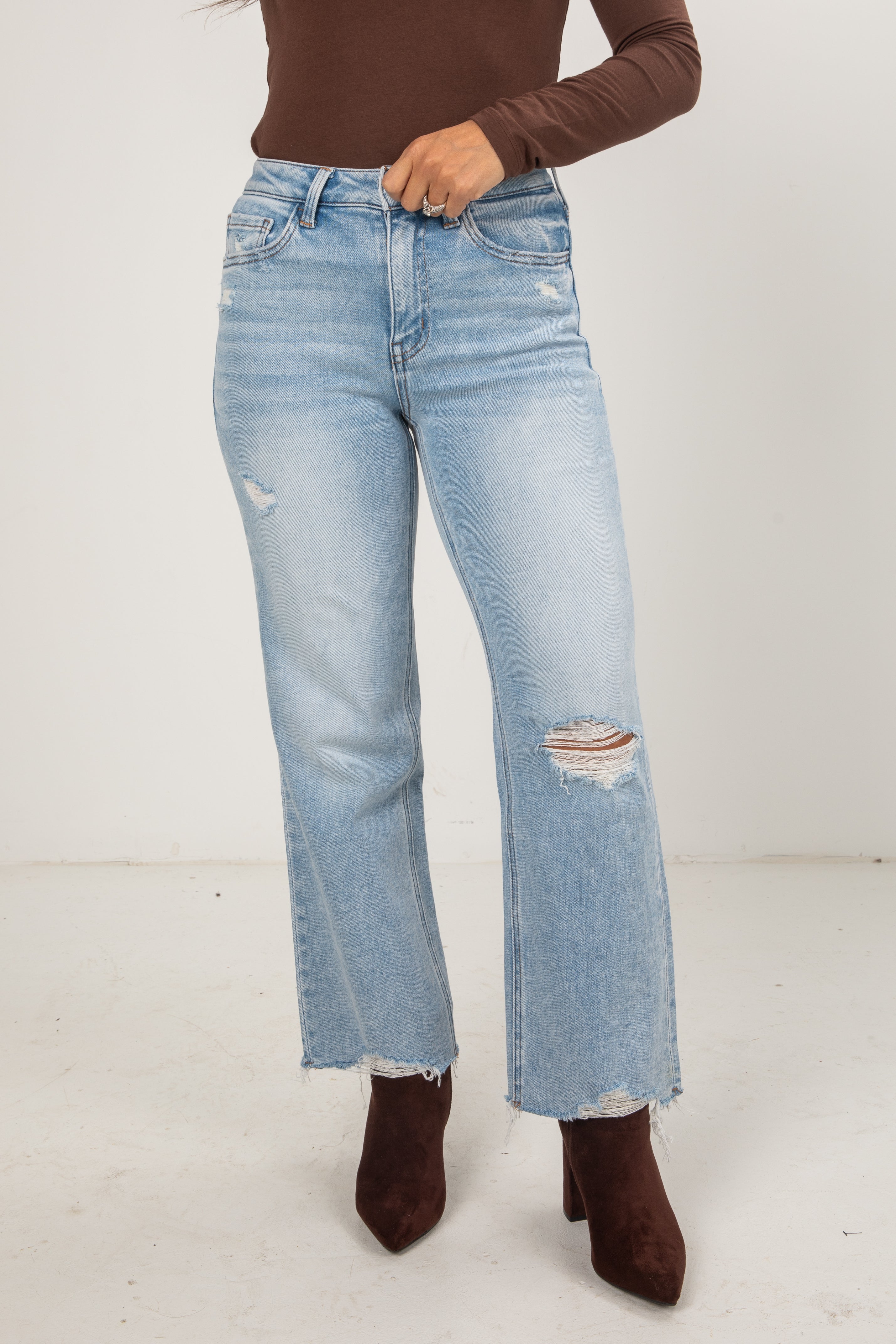 Person wearing light blue jeans with a brown top and shoes on a white background