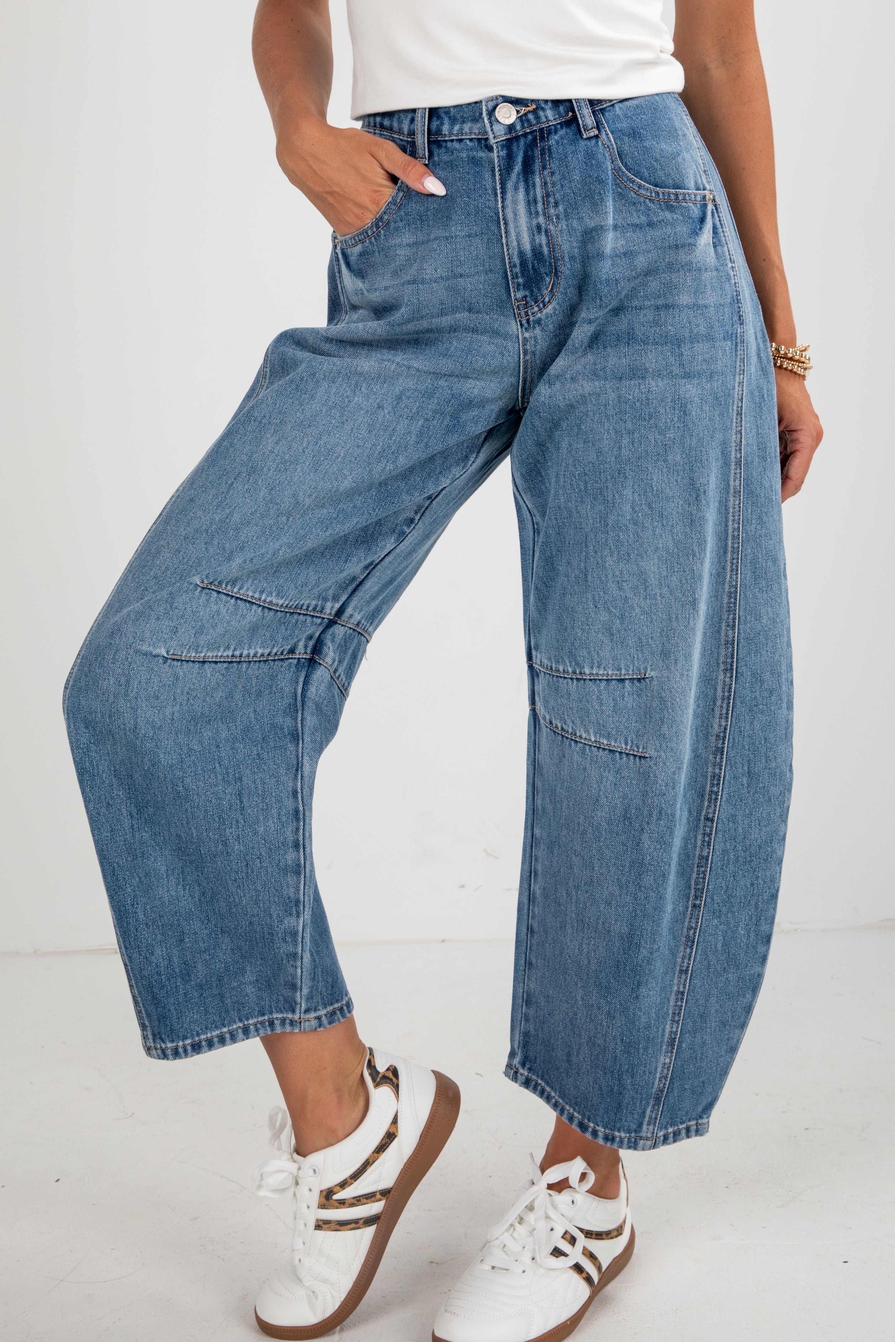 Person wearing blue wide-leg jeans and white sneakers on a white background