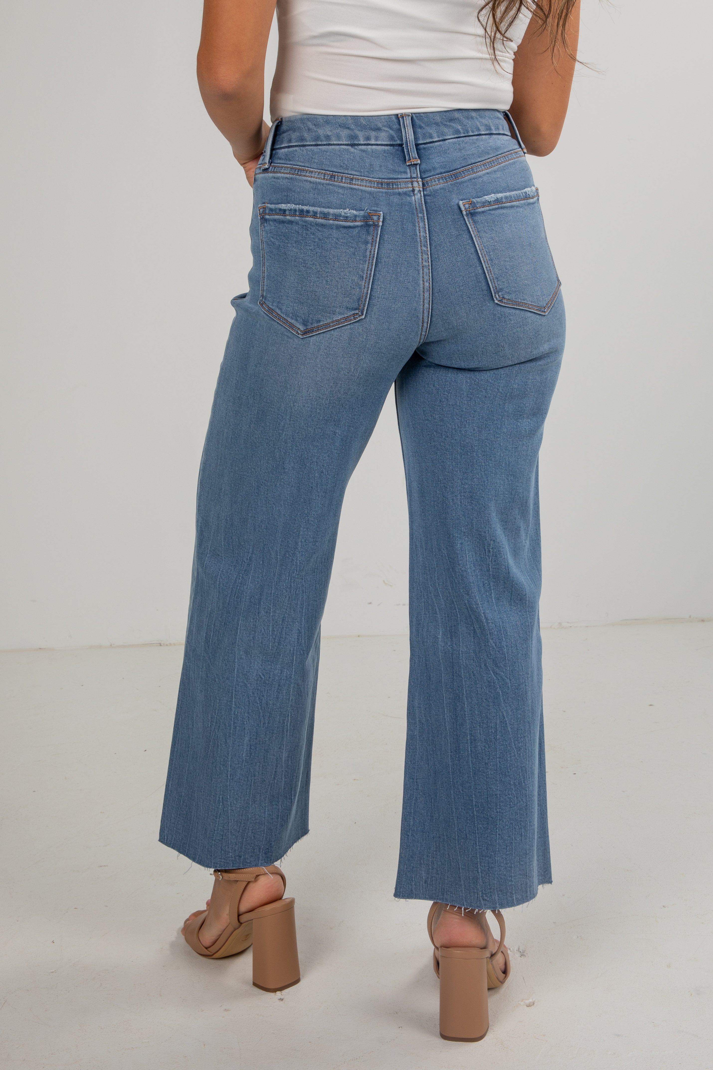 Person wearing blue jeans and a white top on a plain background