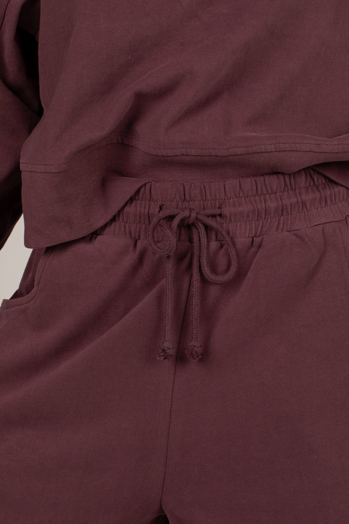 Close-up of a matching lounge set in a deep plum-burgundy color, featuring a drawstring waist on the pants and a soft, slightly wrinkled texture.