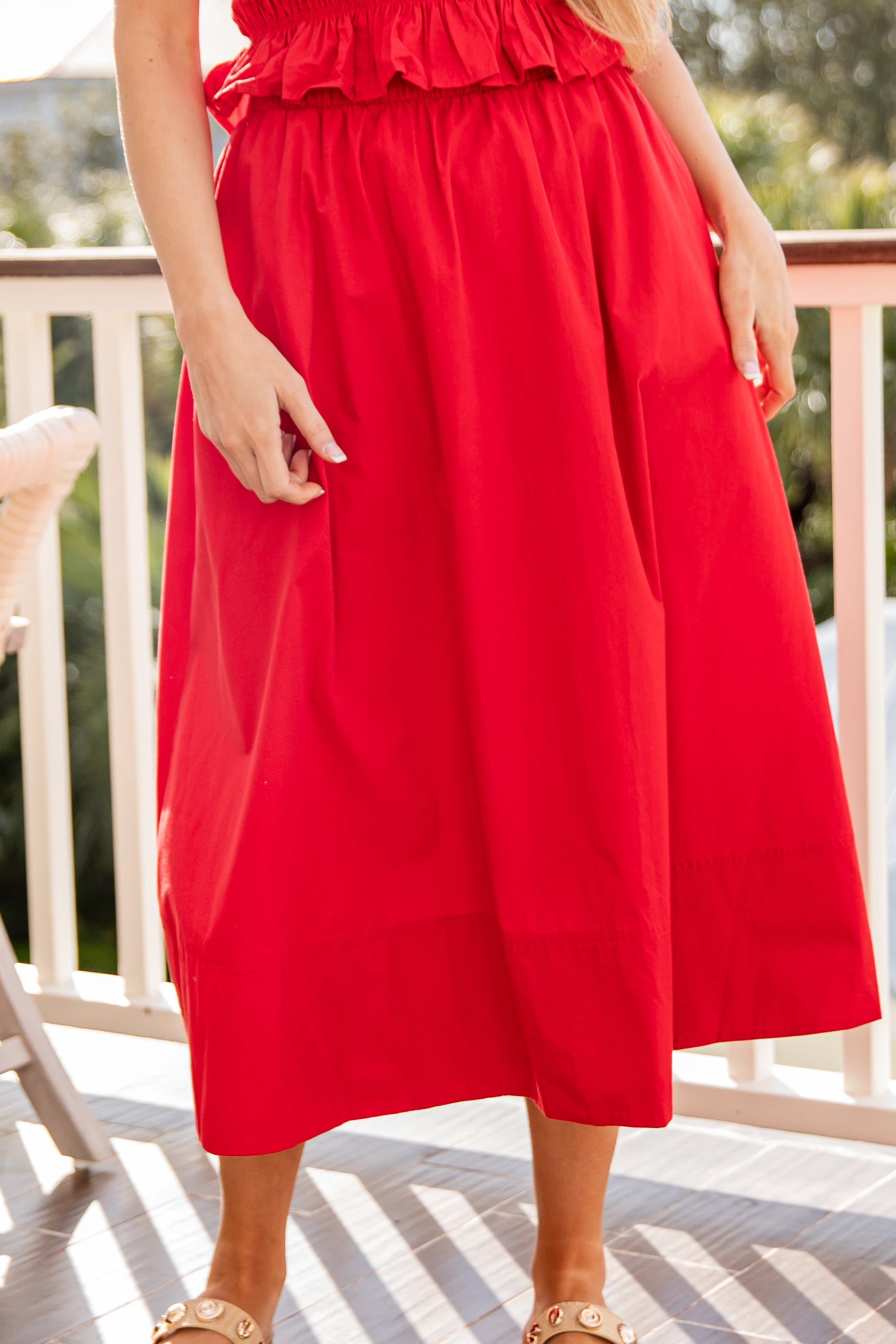 Person wearing a red dress on a balcony with greenery in the background