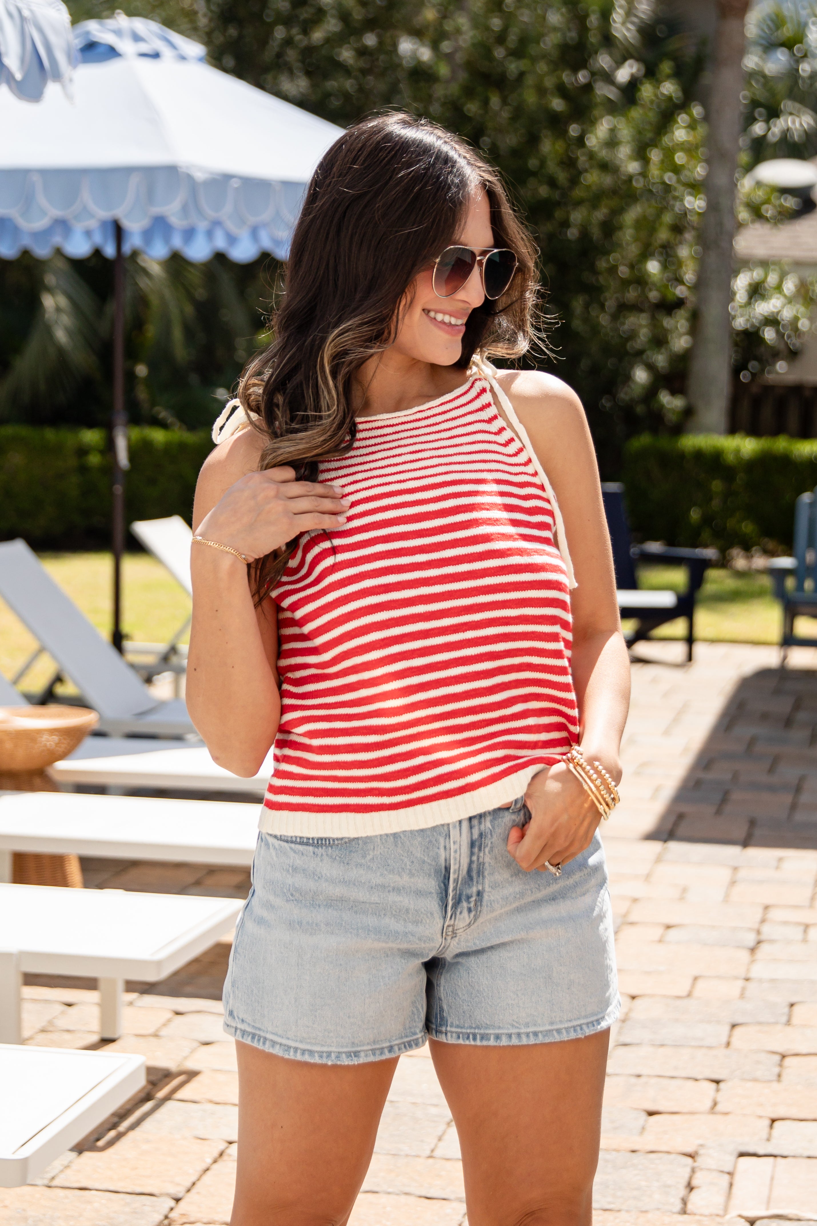 Woman wearing a red and white striped tank top and denim shorts standing outdoors.
