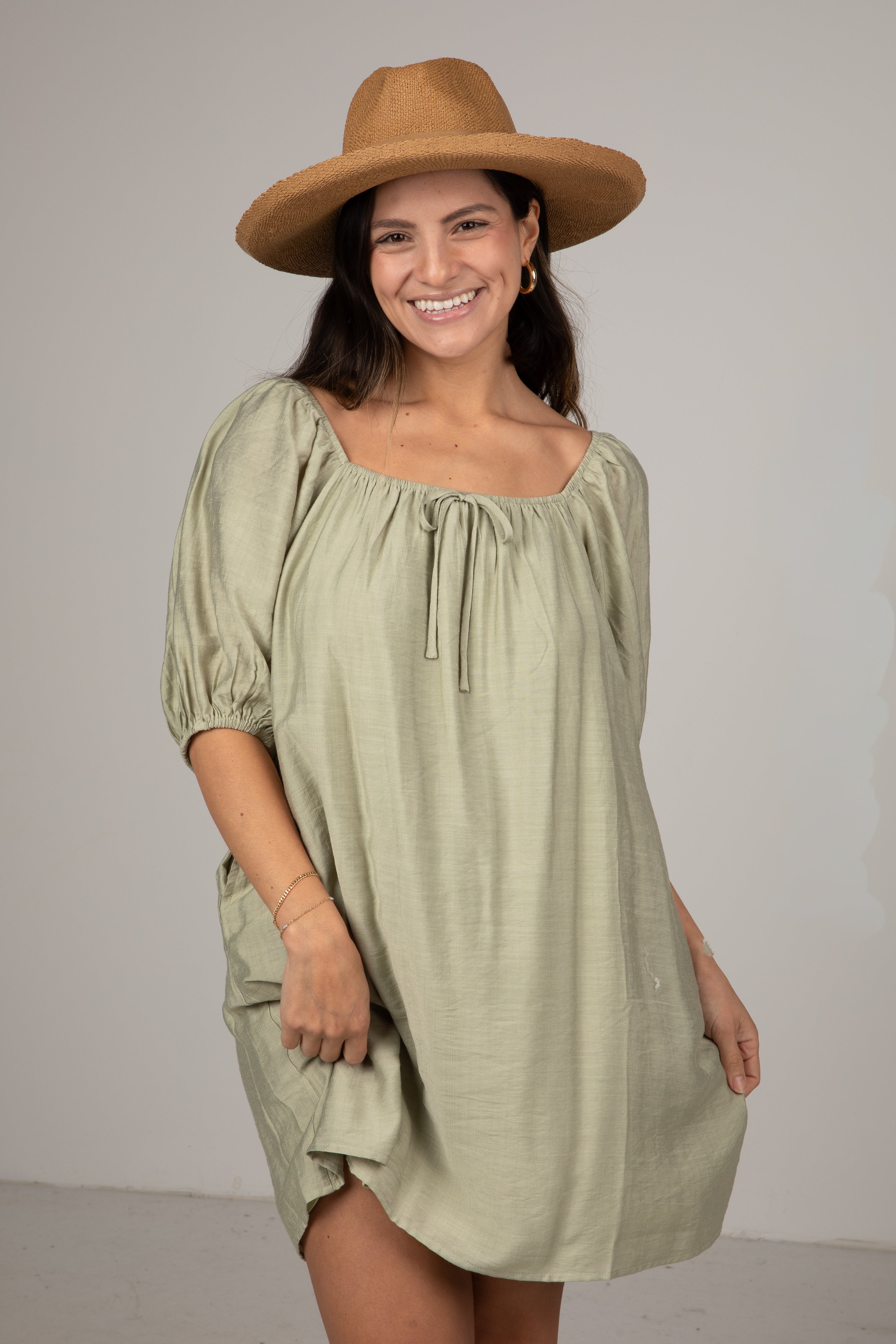 Woman wearing a green dress and brown hat against a plain background