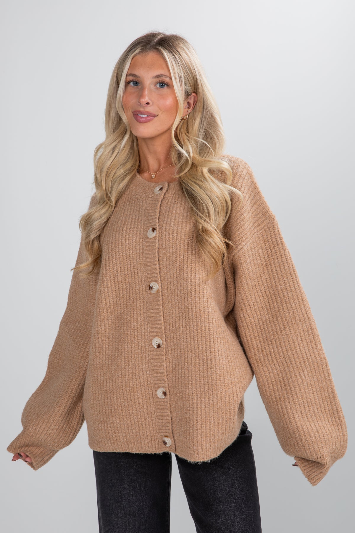 Woman wearing a beige ribbed sweater against a plain background