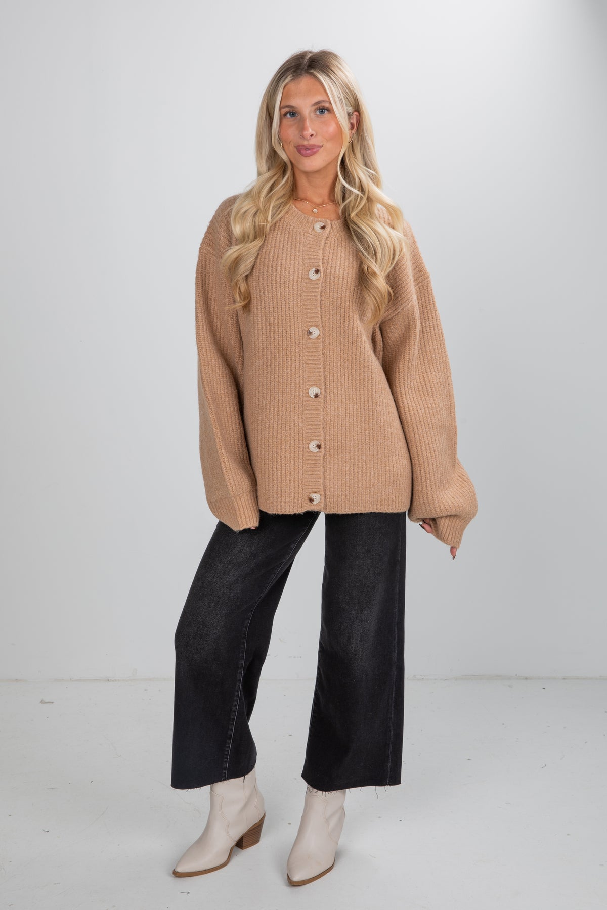 Woman wearing a beige cardigan, black pants, and white boots on a white background