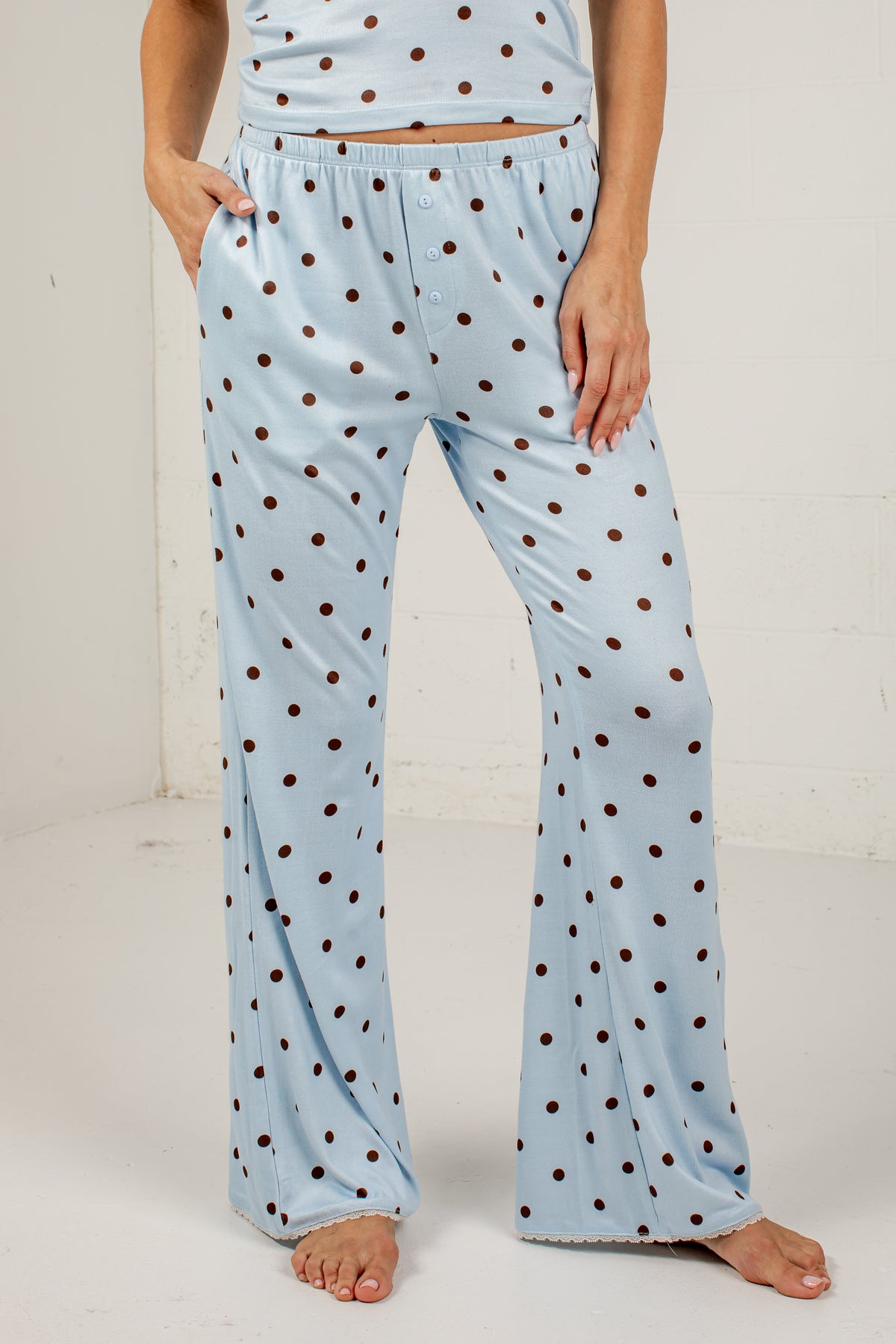 A person wearing light blue flared pajama pants with dark brown polka dots, shown from the waist down against a plain white studio background.