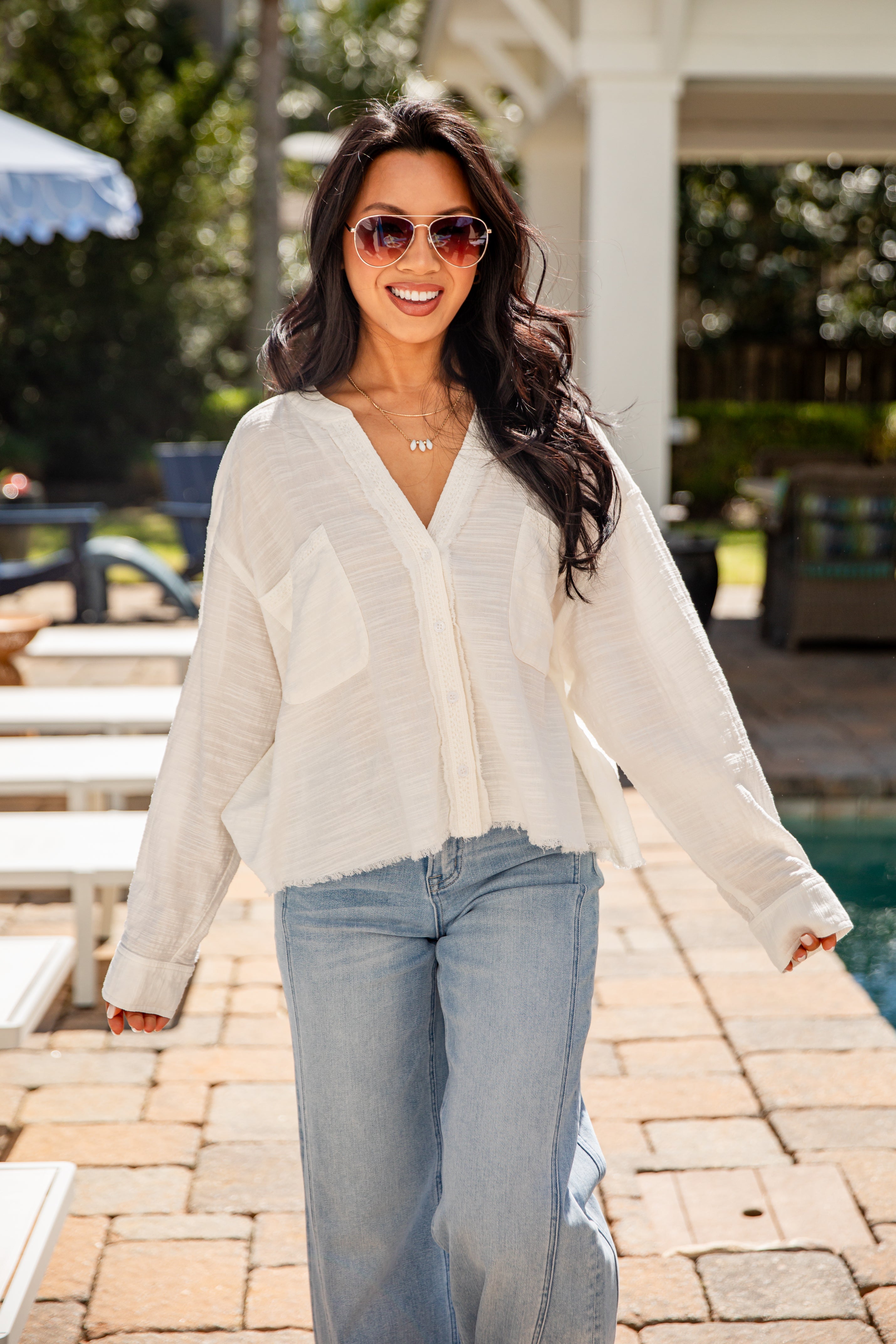Woman wearing a white blouse and blue jeans standing by a poolside.