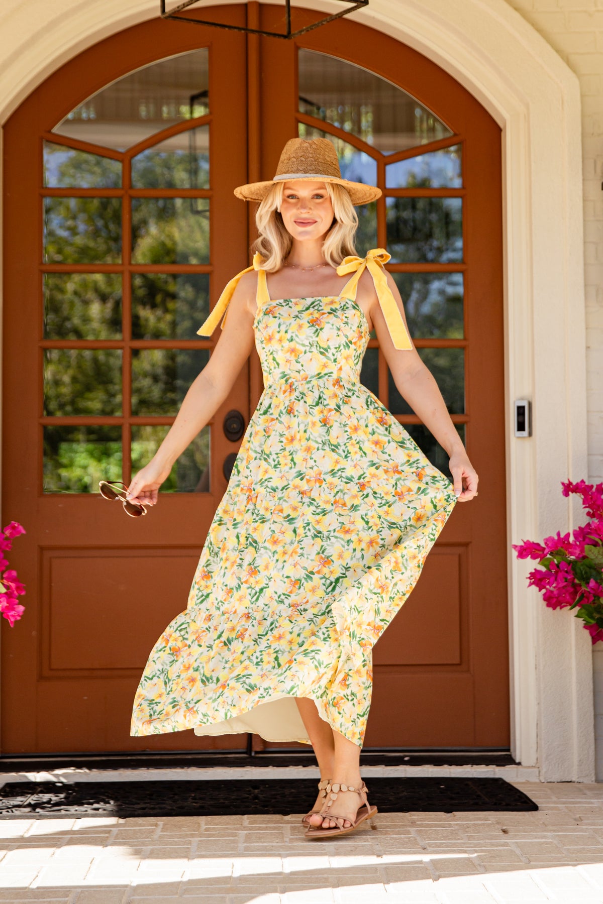 Woman in a floral dress with yellow accents standing in front of a brown door.