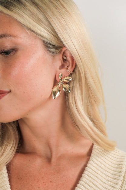 Close-up of a woman wearing gold leaf-shaped earrings against a neutral background