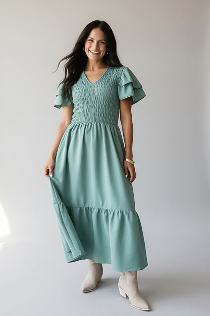 A woman wearing a sage green tiered maxi dress with ruffled short sleeves and smocked detailing