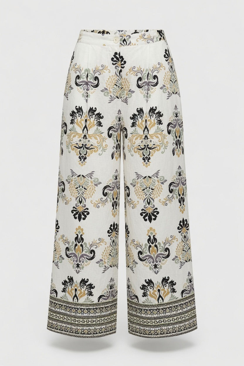 White wide-leg cropped pants with a black and beige baroque-style damask pattern and a decorative border on the hems, shown against a light gray background.