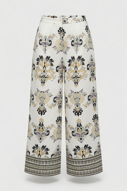 White wide-leg cropped pants with a black and beige baroque-style damask pattern and a decorative border on the hems, shown against a light gray background.