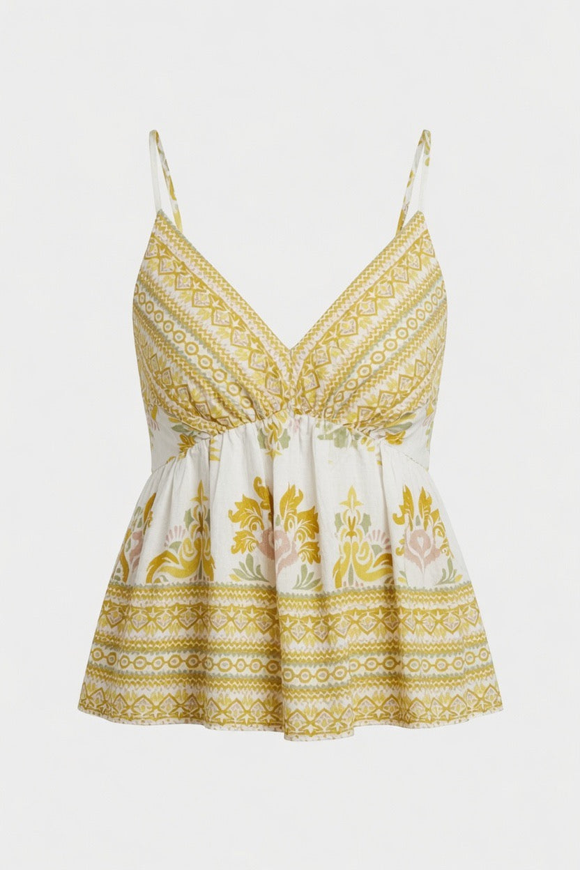 A sleeveless bohemian-style camisole top with thin straps, a V-neckline, and a gathered peplum waist. The fabric features a white base with yellow-gold geometric patterns and a central floral print in yellow, pink, and green, set against a plain light gray background.
