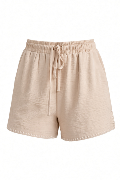 Beige textured drawstring shorts with an elastic waistband, photographed against a plain white background.