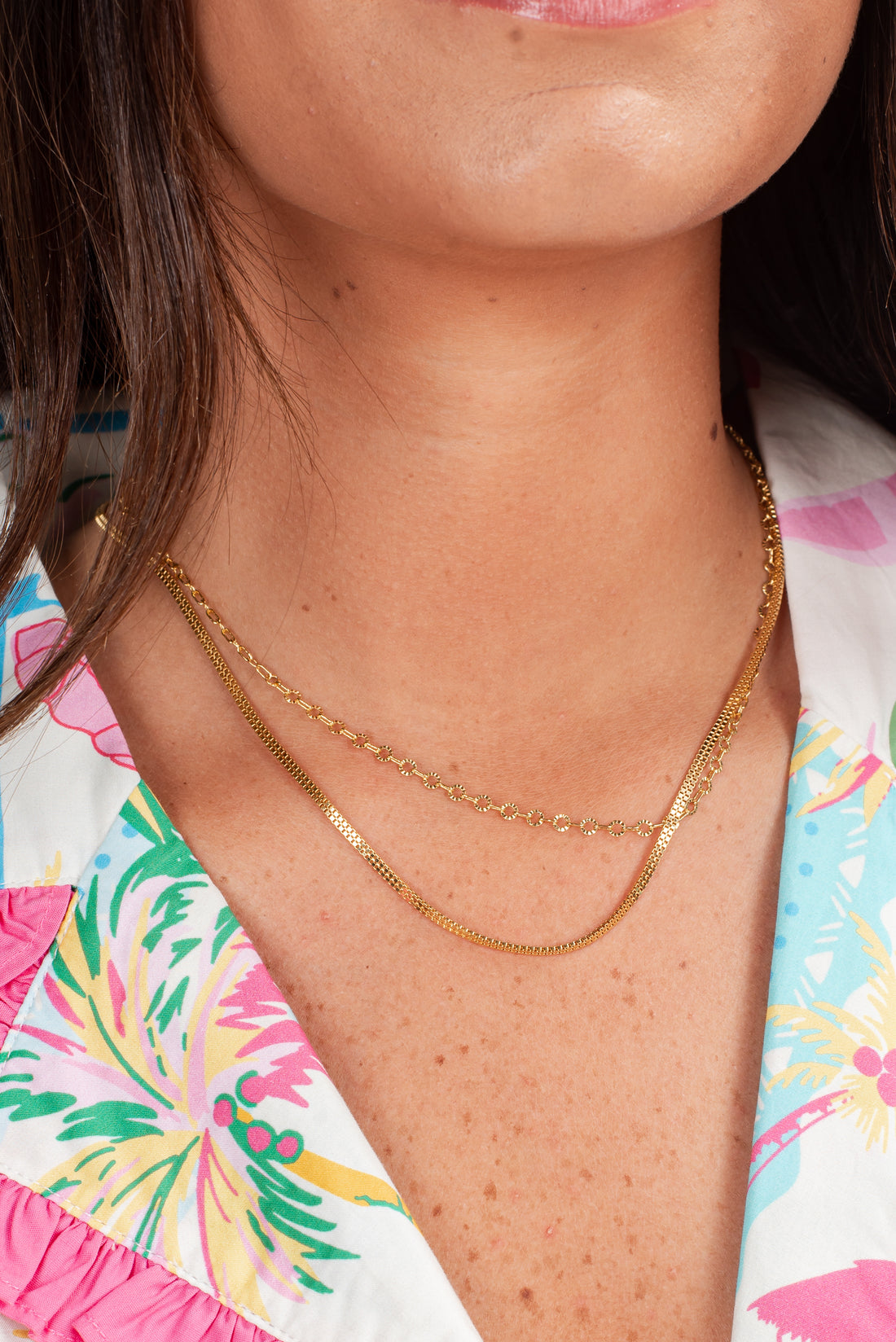 Close-up of a person wearing a gold necklace with a colorful shirt in the background