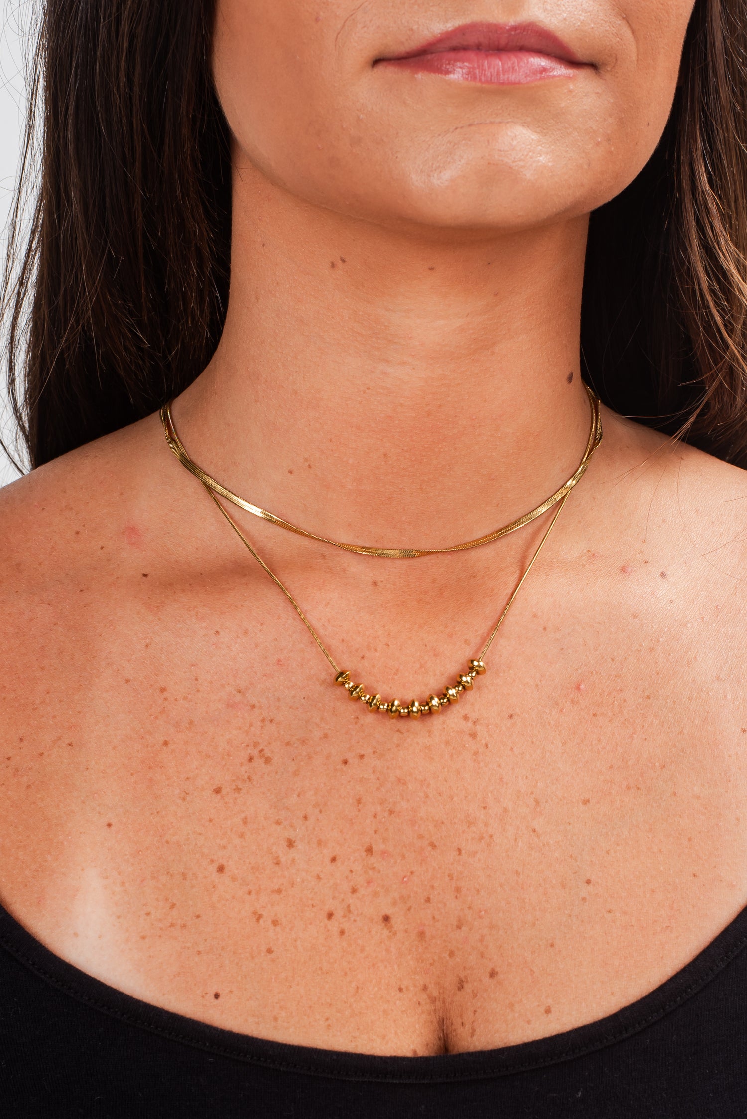 Close-up of a person wearing a gold necklace with a plain background