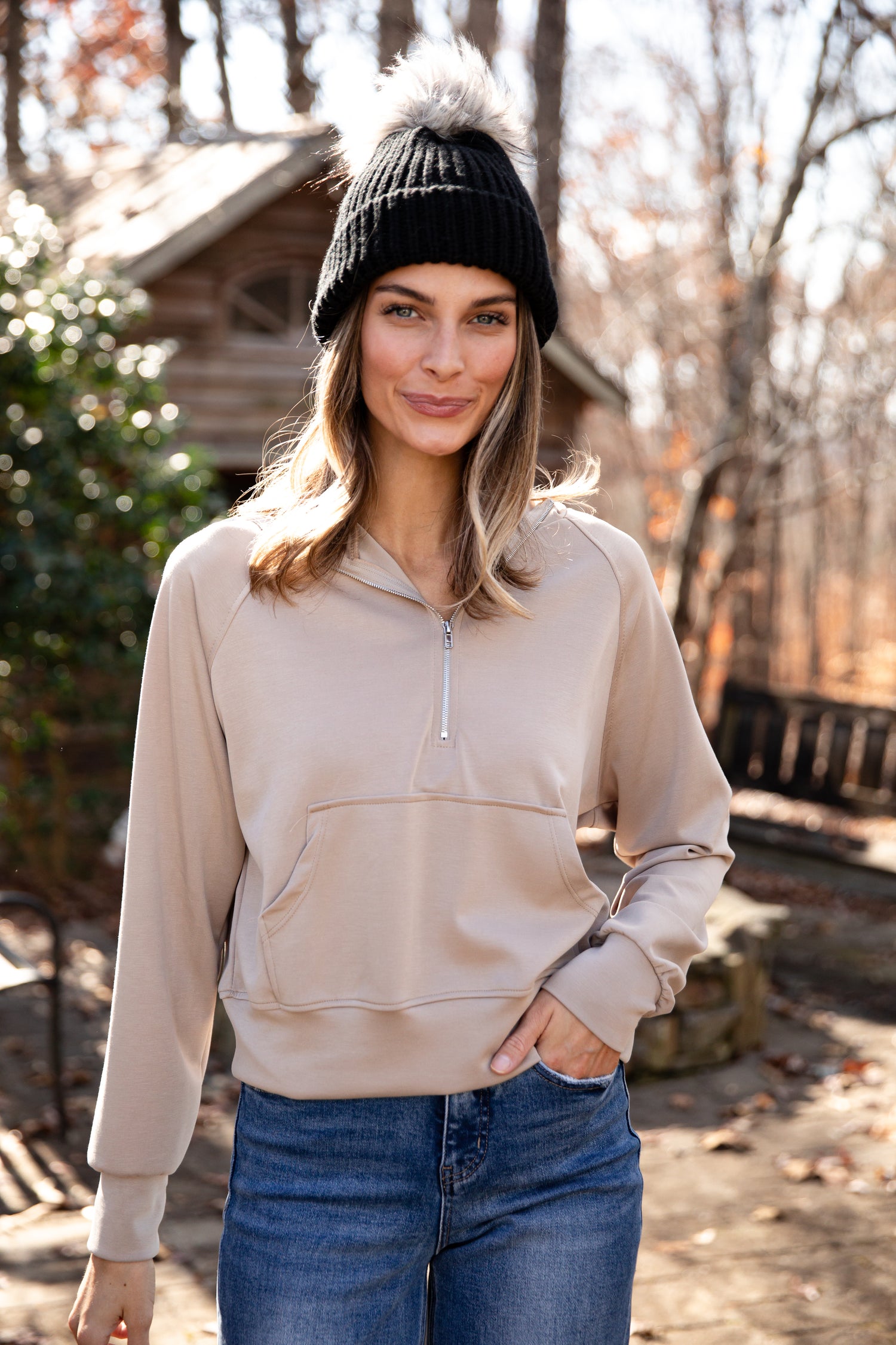 Woman wearing a beige half-zip sweatshirt and black beanie outdoors.