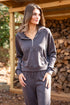 Woman wearing a gray tracksuit standing in front of stacked firewood.