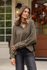 Woman wearing a green blouse and dark jeans standing on a porch.