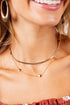 A close-up lifestyle shot of a woman wearing a double-layered gold necklace. The necklace features a thin curved band on the top layer and a delicate chain with three small gold bead pendants on the bottom layer.